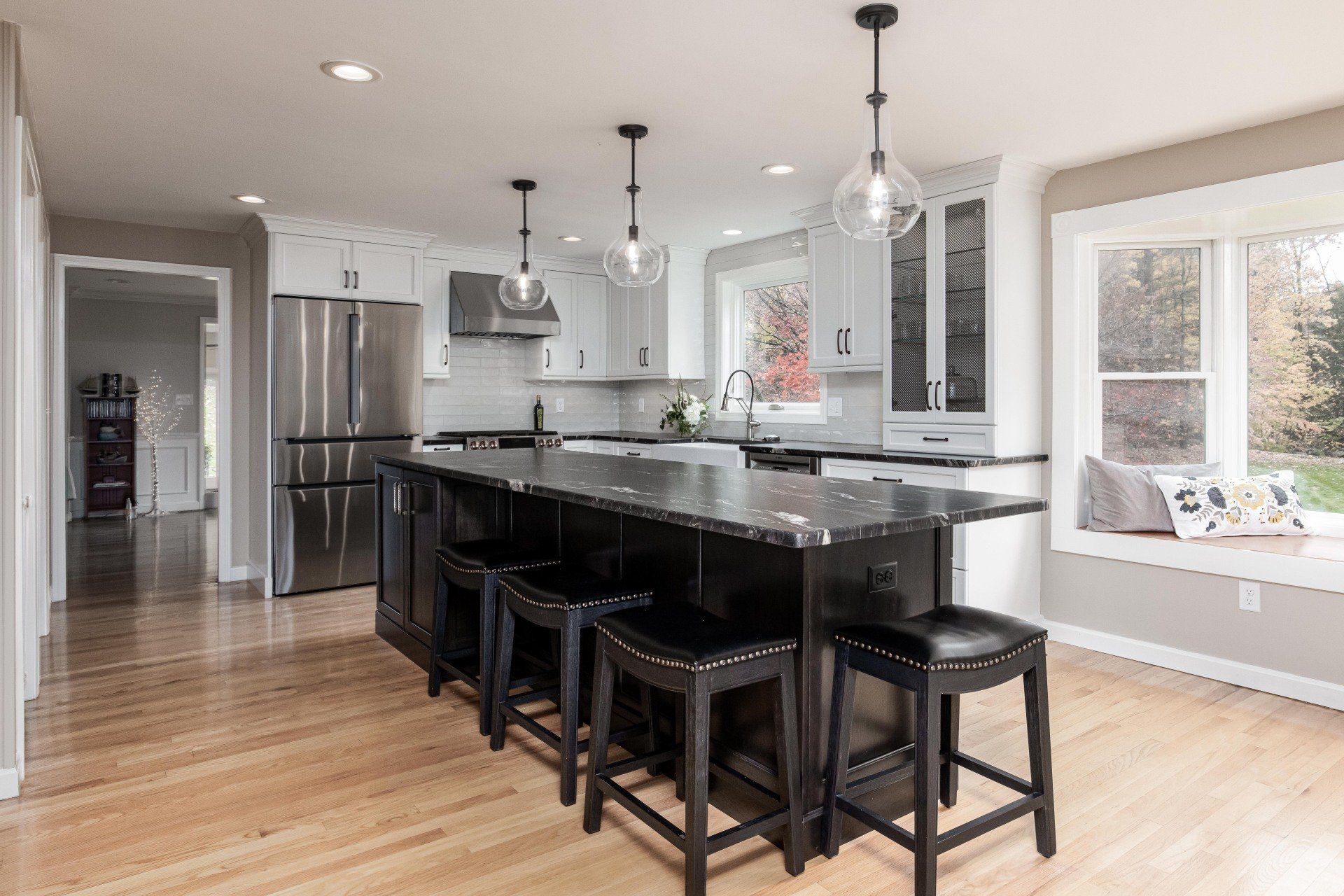 Bright modern kitchen with black island stools, stainless appliances, and hardwood floors