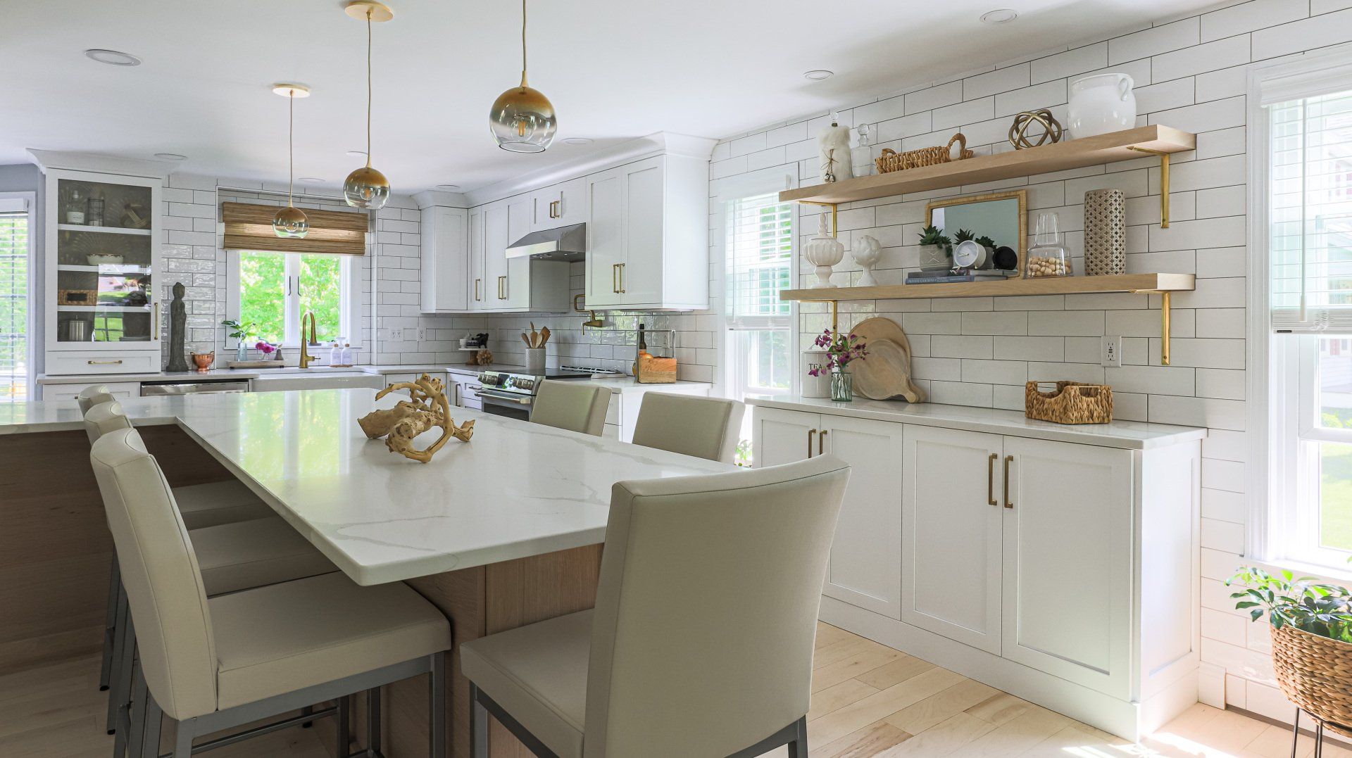 Bright white kitchen-dining room with a long table, upholstered chairs, and open shelves by a window.