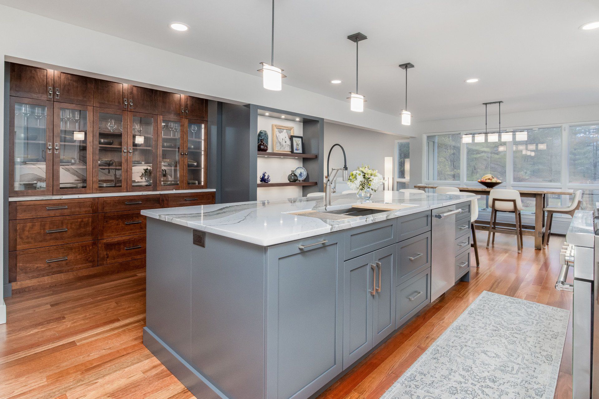 Modern kitchen with gray island, white countertops, wood floors, and dining area by windows