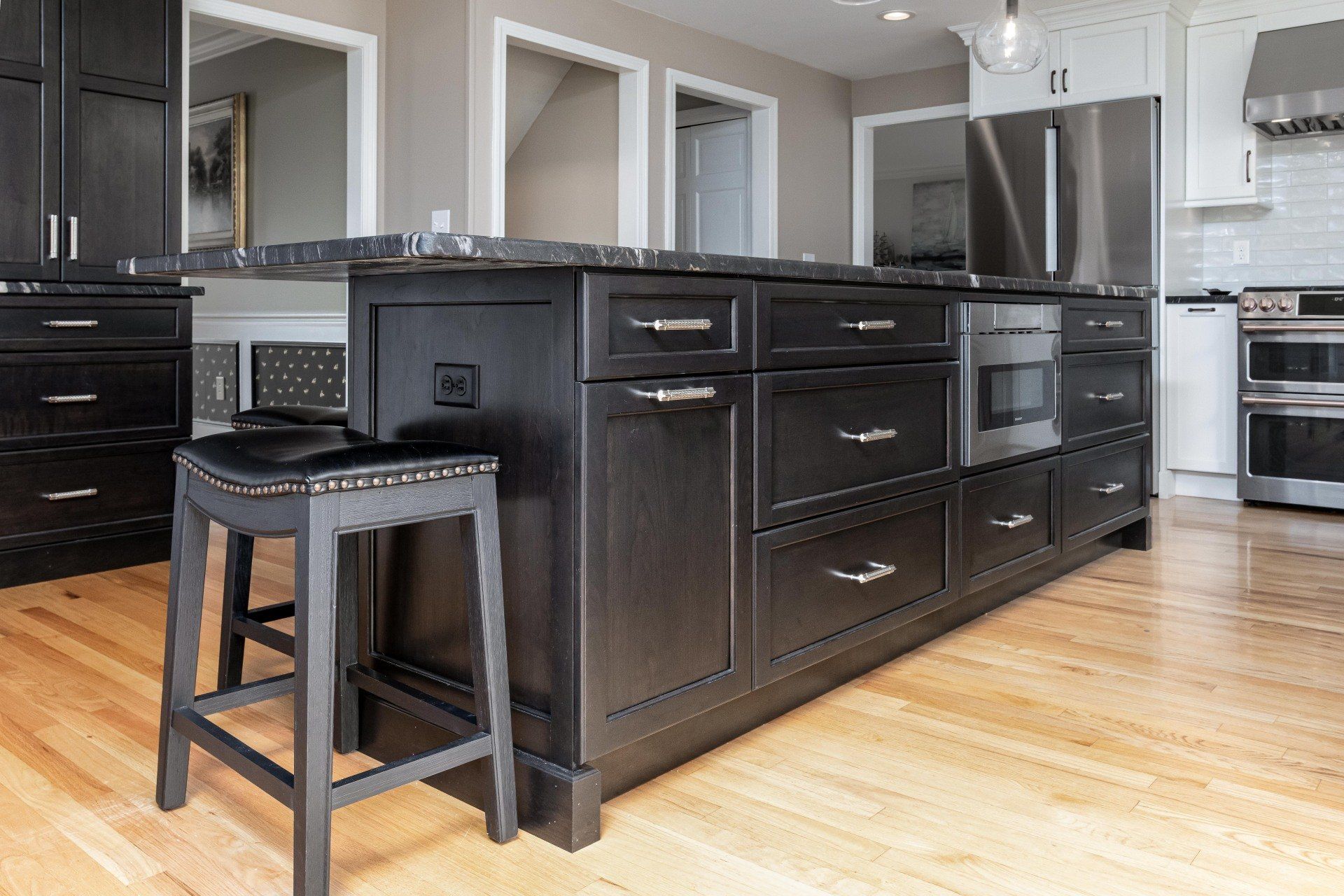 Modern kitchen with dark island, black stool, stainless steel appliances, and light wood floors