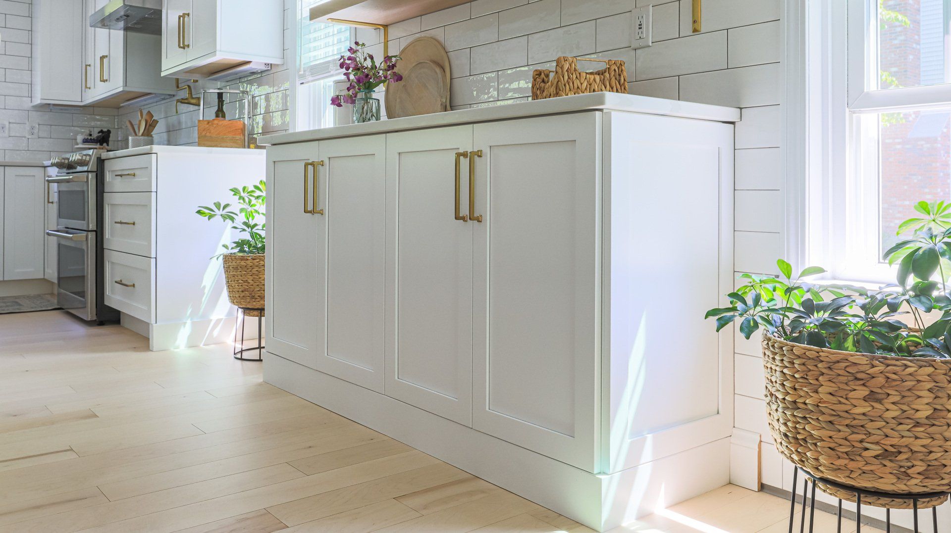 Bright white kitchen with gold accents, potted plants, and sunlight by a window