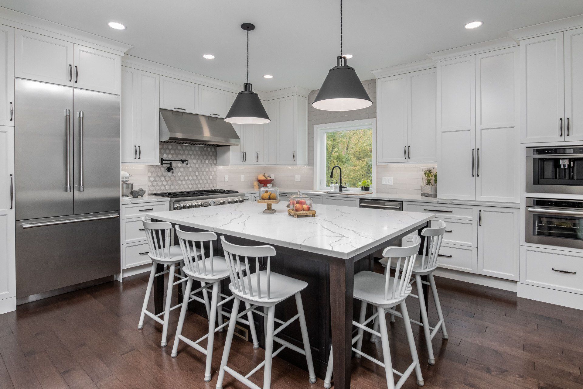 Bright modern white kitchen with island, bar stools, stainless appliances, and pendant lights