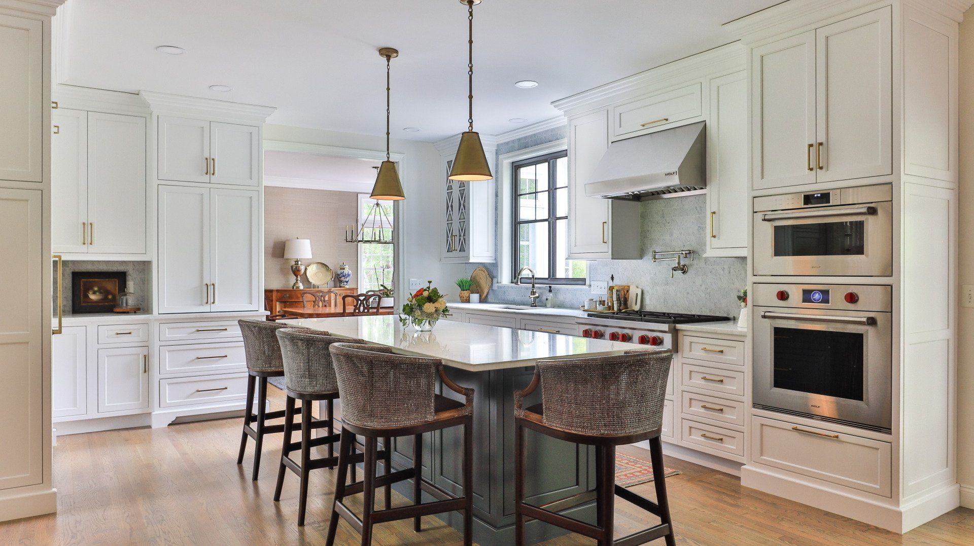 Bright white kitchen with island, pendant lights, marble counters, and built-in ovens.