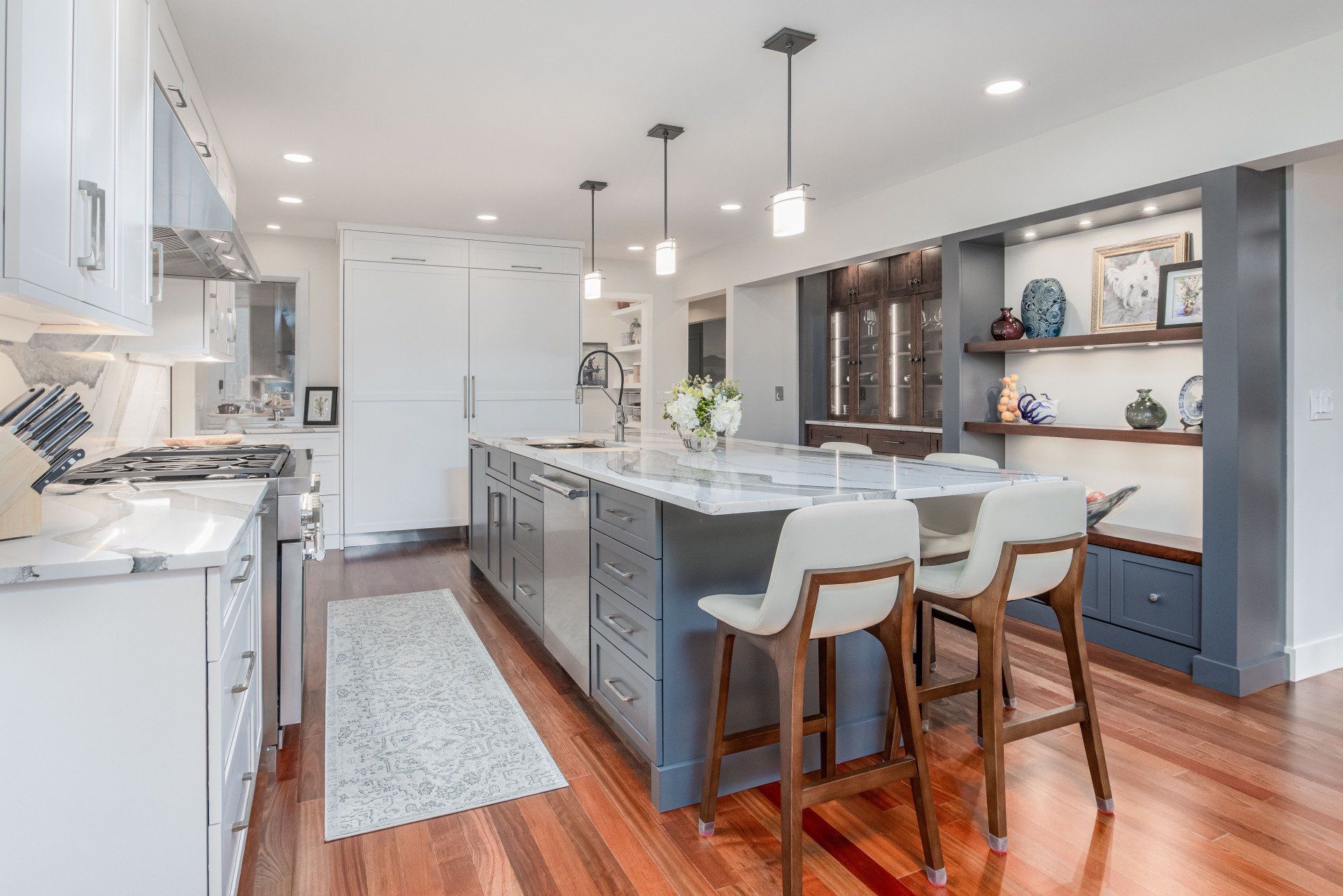 Bright modern kitchen with white cabinets, gray island, wood floors, and three bar stools