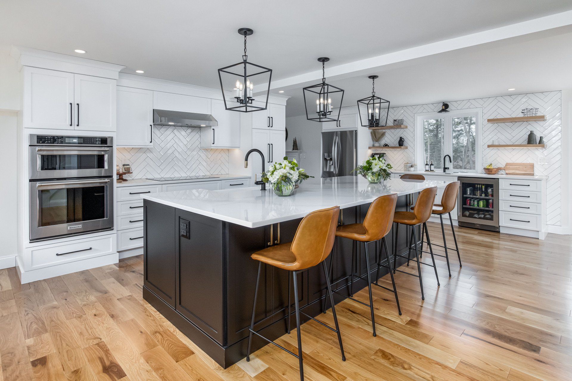 Modern white kitchen with dark island, wooden stools, pendant lights, and hardwood floors