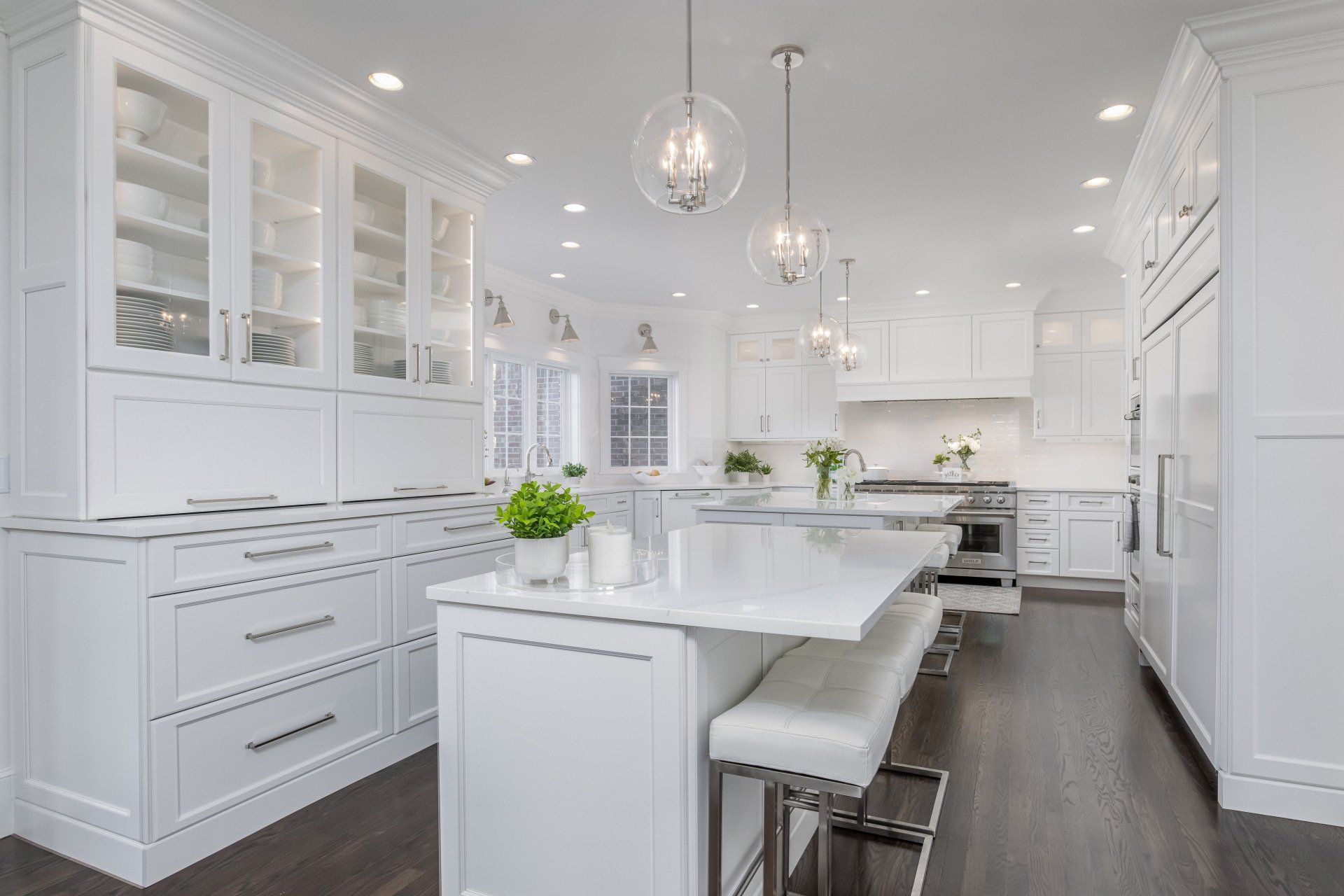 Bright white modern kitchen with island, bar stools, pendant lights, and dark wood floors