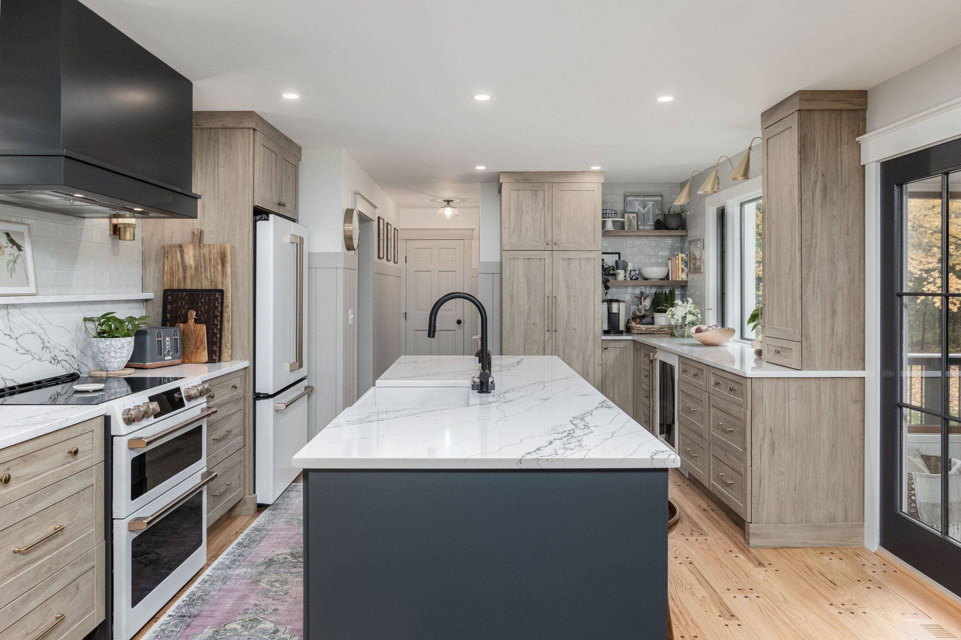 Bright modern kitchen with a large white island, light wood cabinets, and black accents.