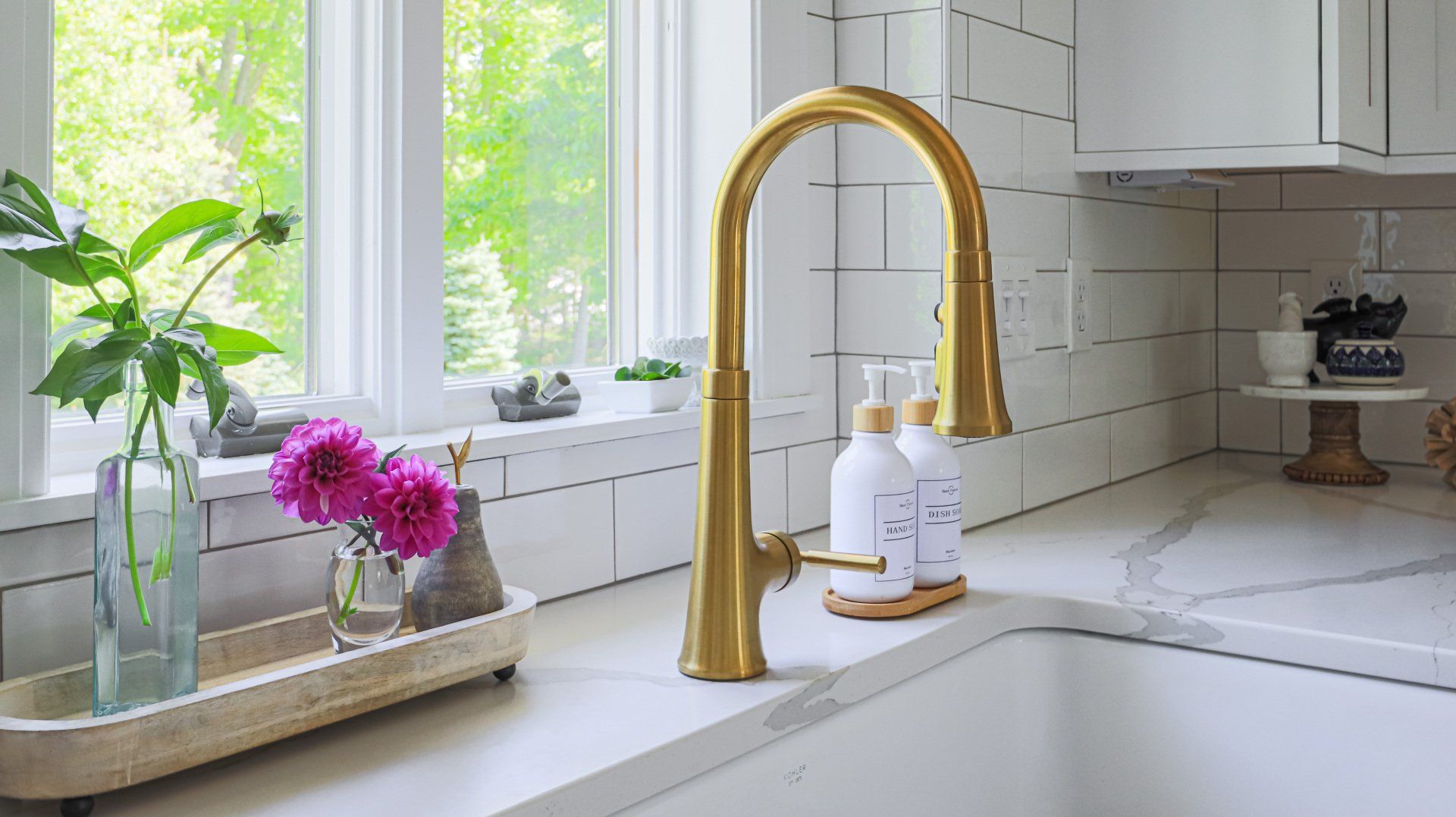 Bright kitchen sink with gold faucet, white countertops, and flowers by a sunlit window
