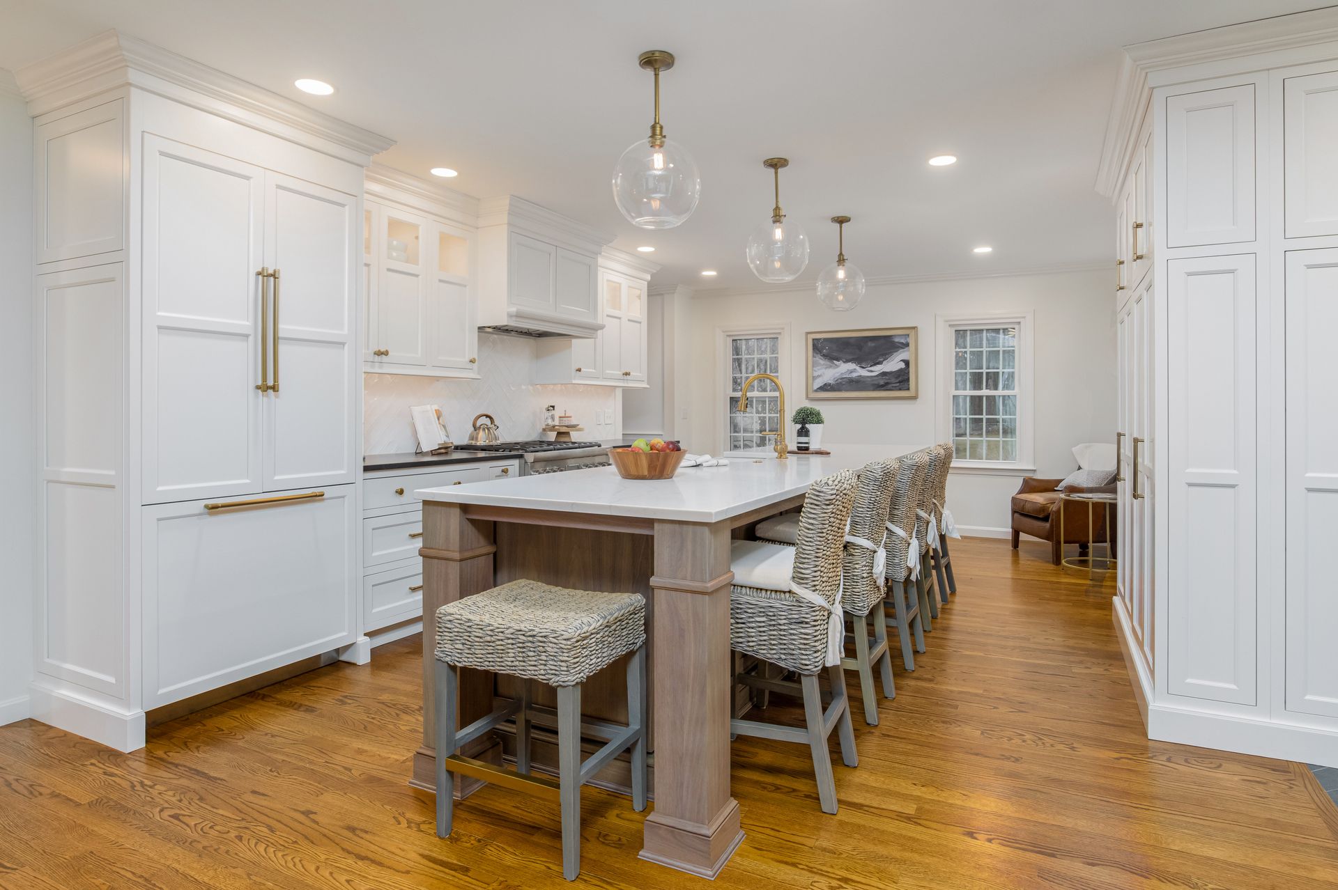 Bright white kitchen with a large island, pendant lights, and bar stools on a hardwood floor.