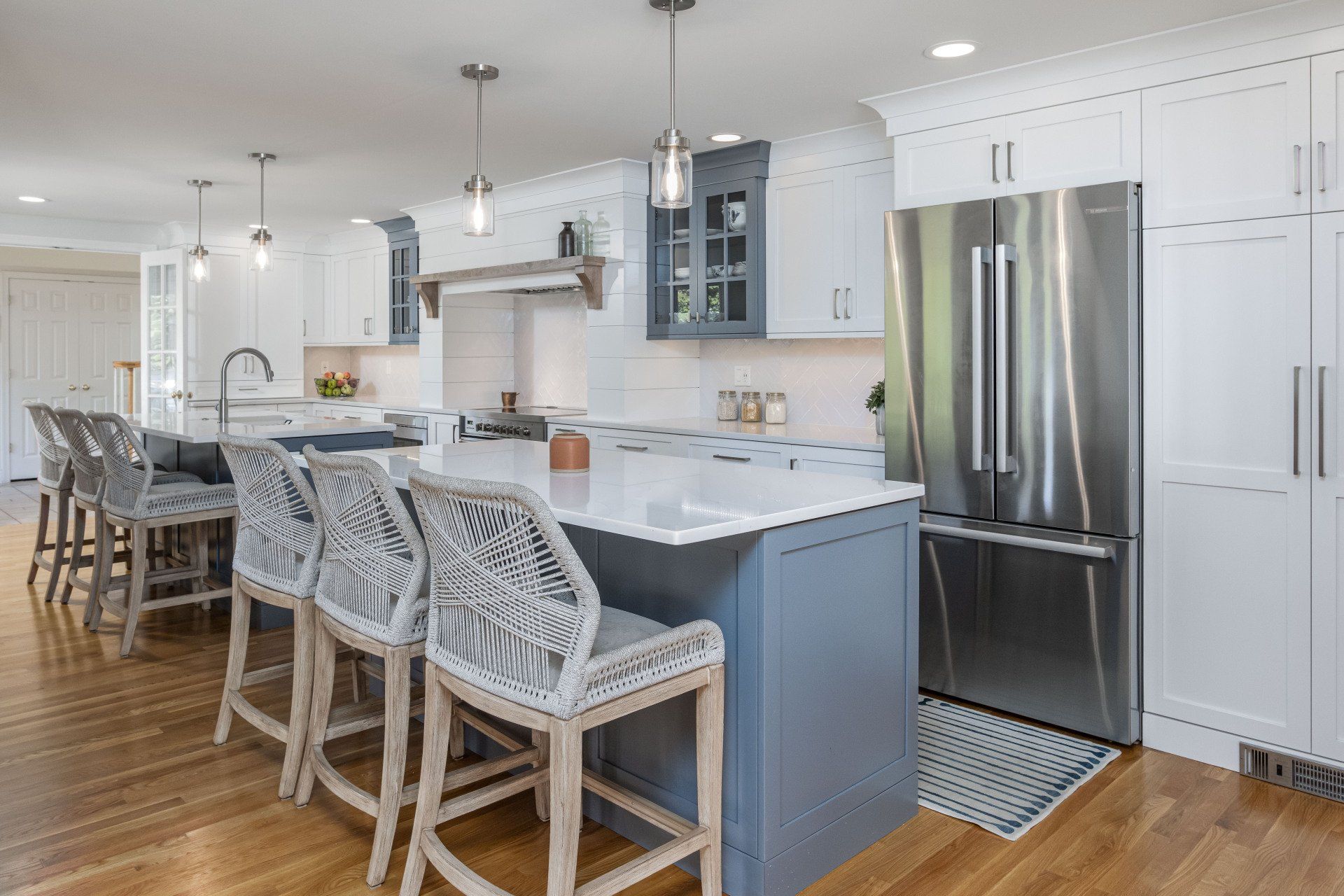 Bright modern kitchen with white cabinets, gray island, bar stools, and stainless steel refrigerator