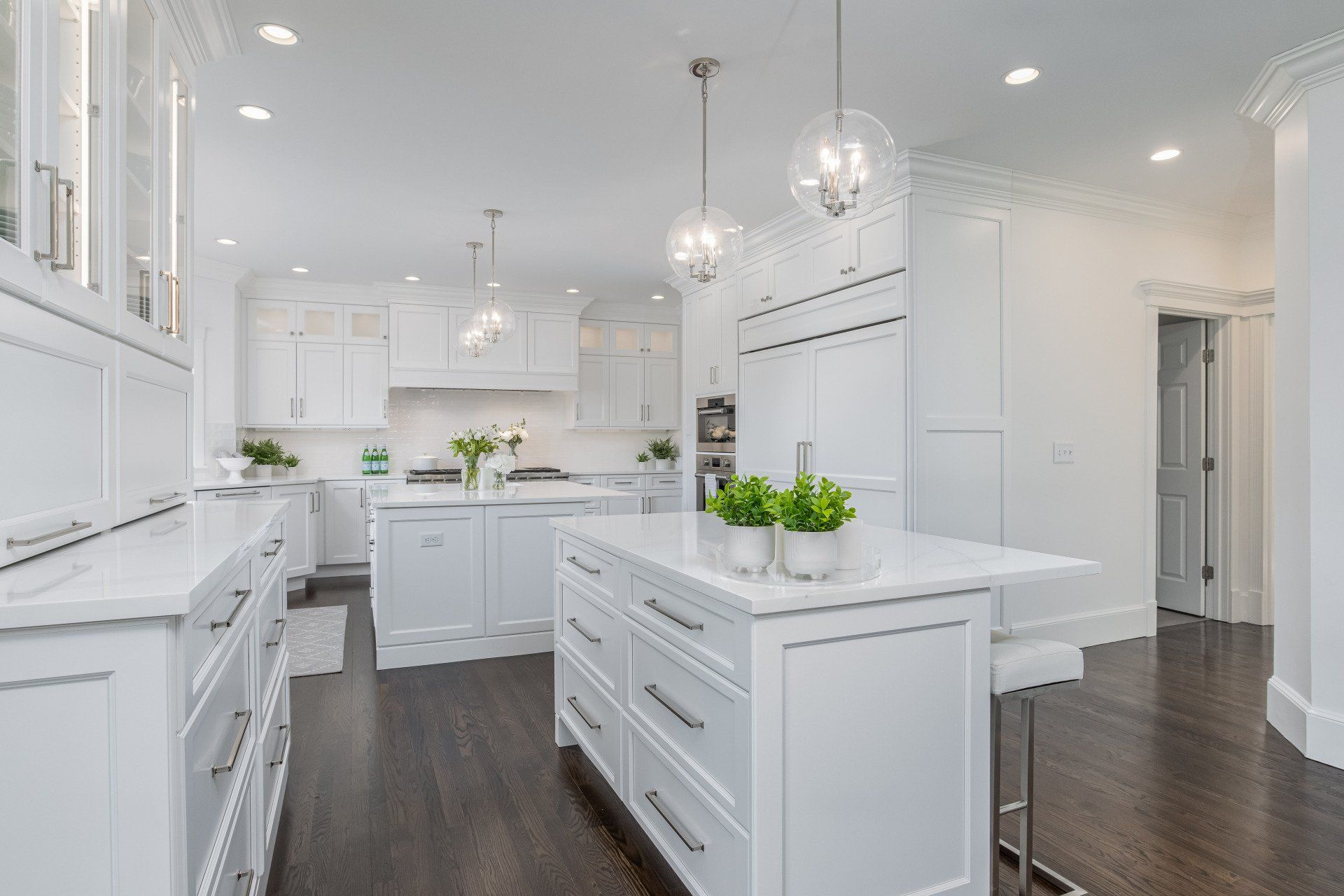 Bright white modern kitchen with island, dark wood floors, and stainless steel appliances