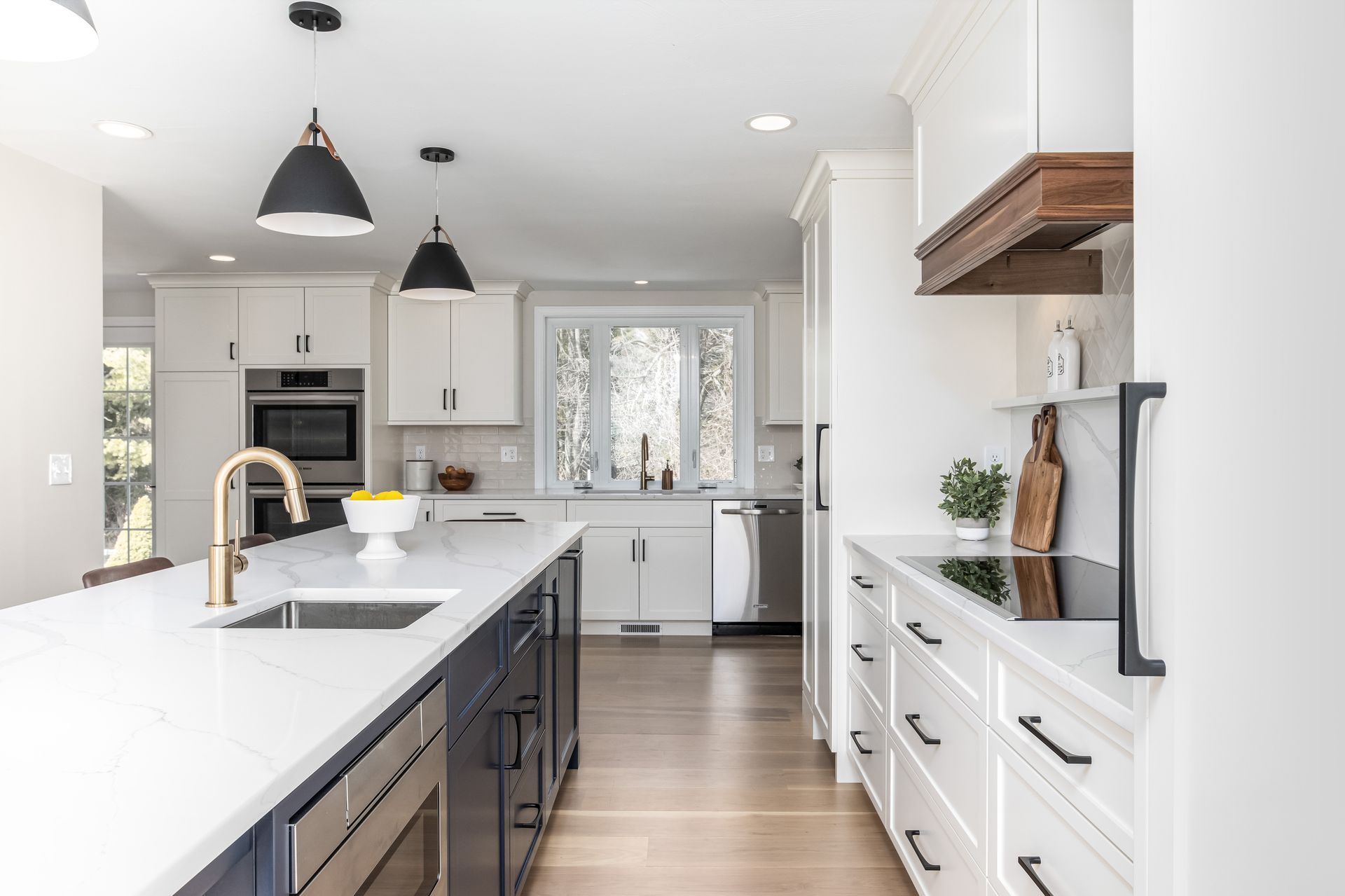 Bright modern kitchen with white cabinets, black island, pendant lights, and wood floors
