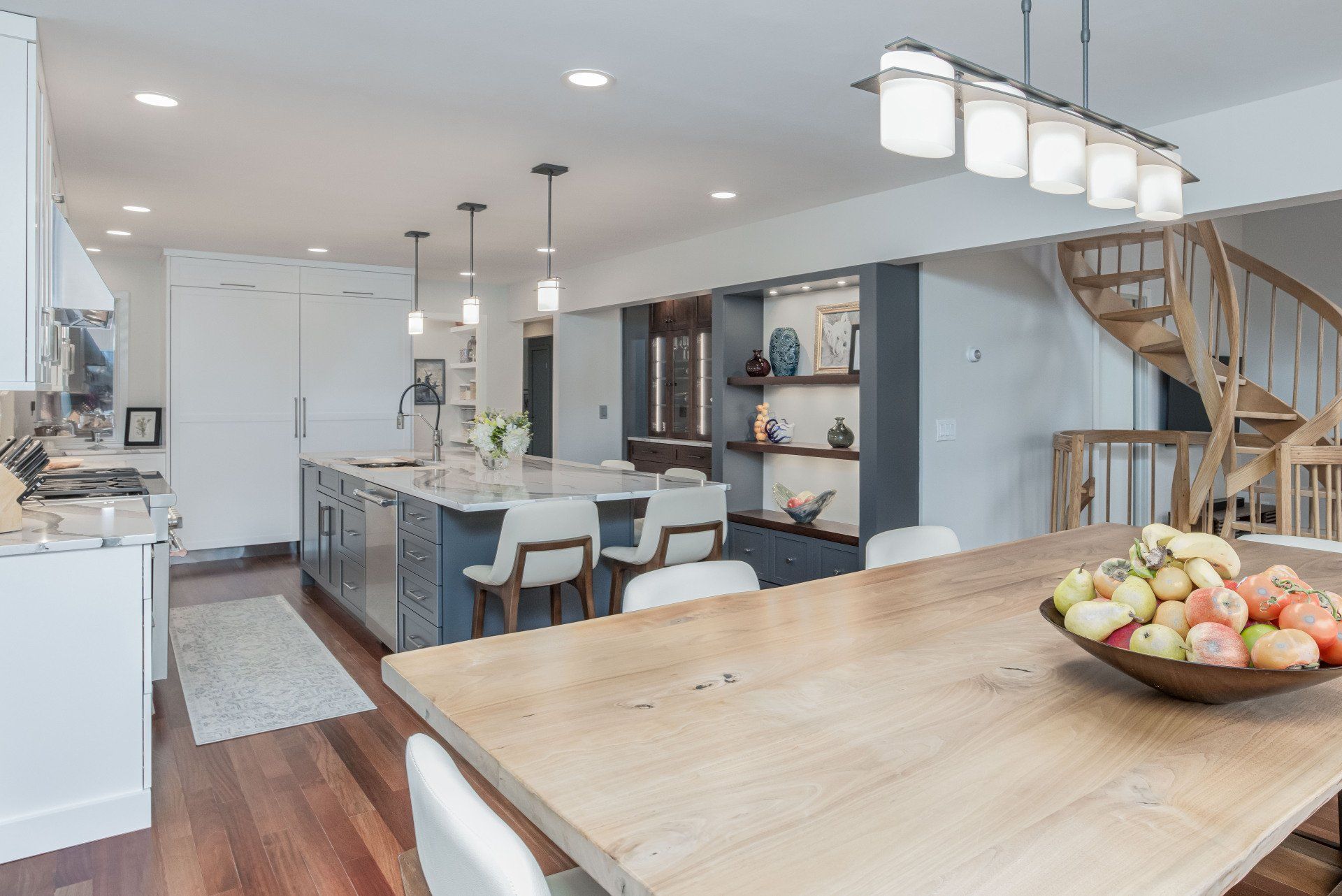 Bright open kitchen and dining area with island, pendant lights, and wooden staircase