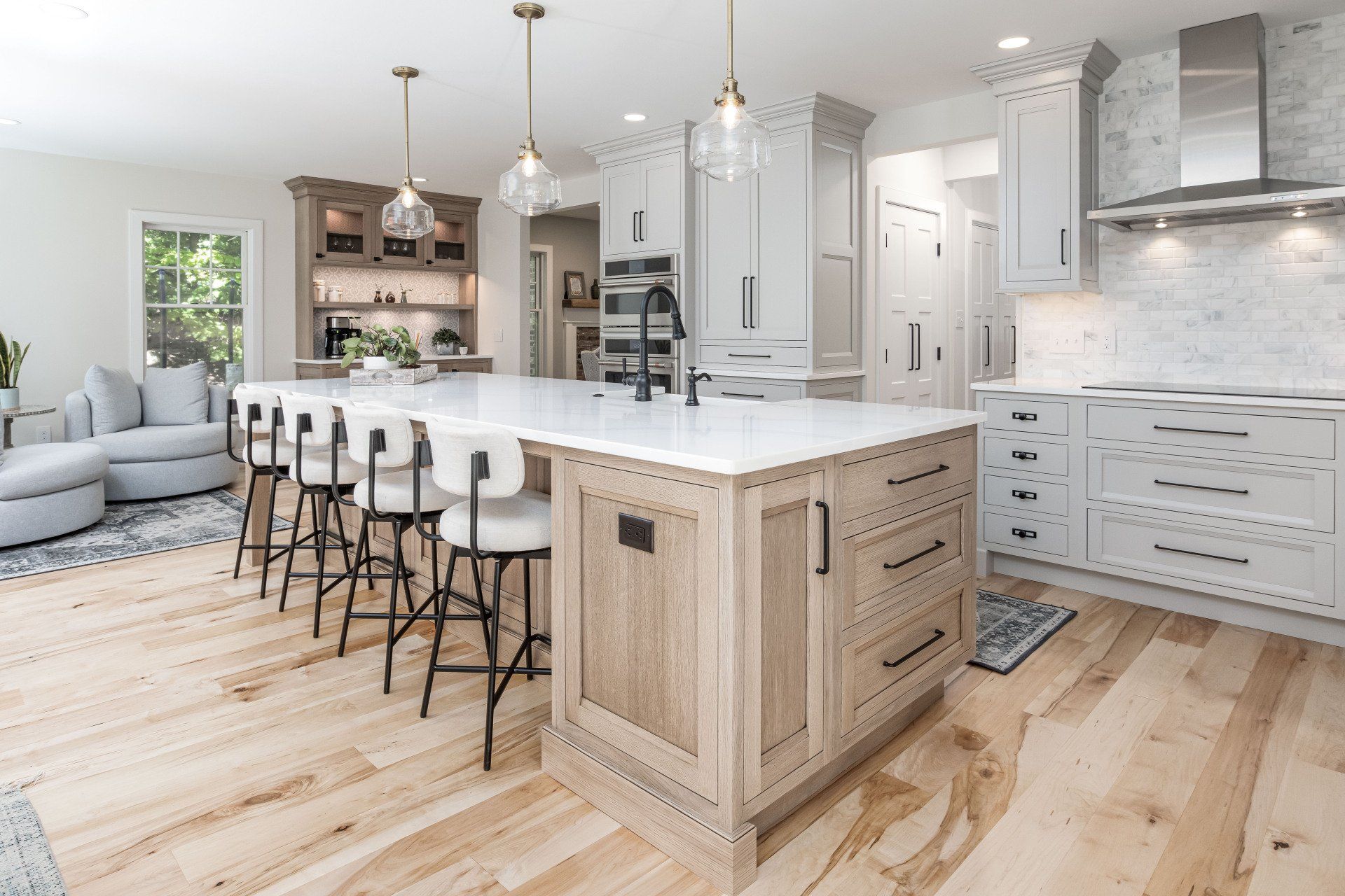 Bright modern kitchen with white cabinets, marble island, barstools, and light wood floors