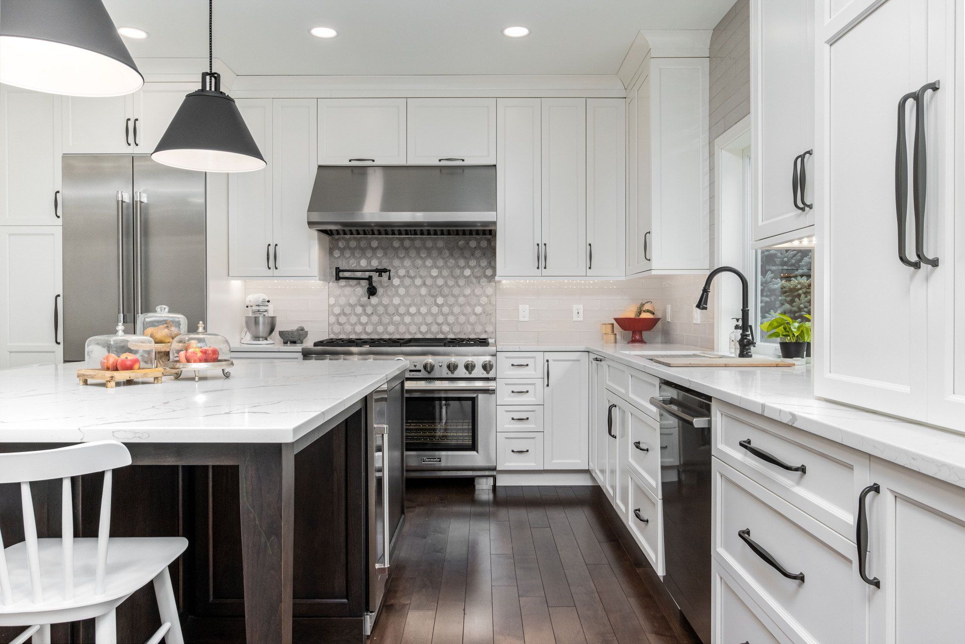 Modern white kitchen with stainless steel appliances, dark wood floor, and marble island counter