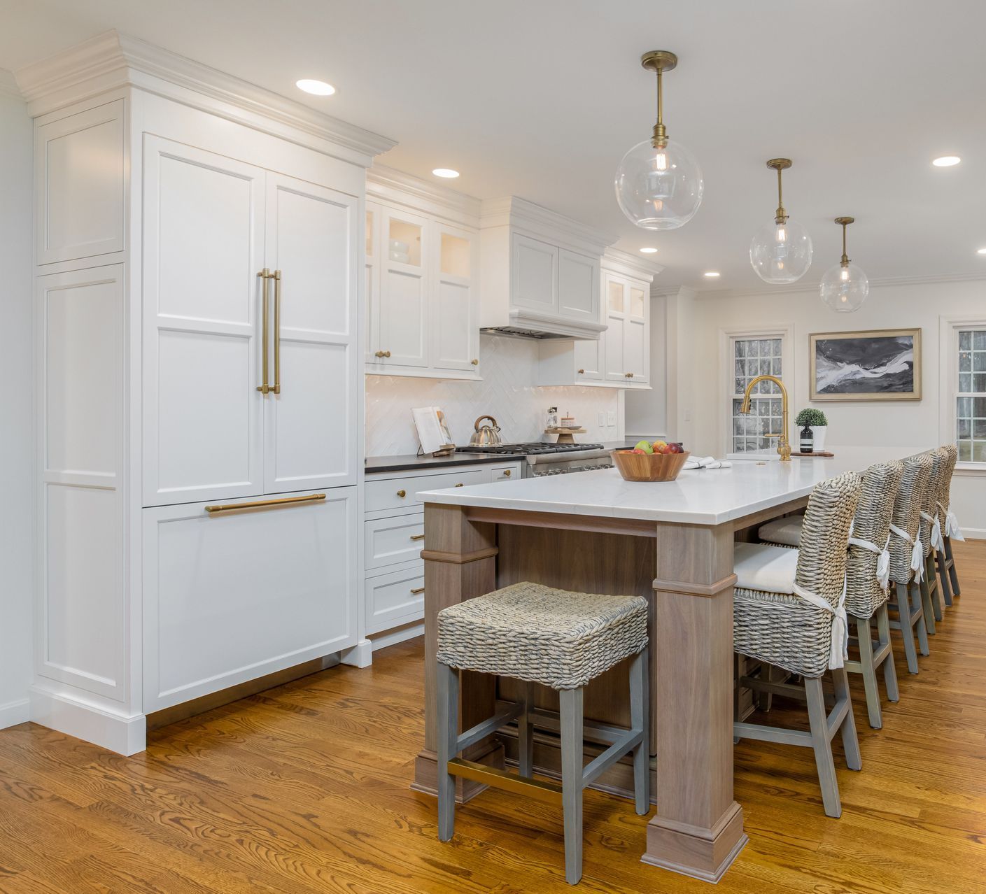 Bright white kitchen with island, pendant lights, and patterned stools on a warm wood floor.