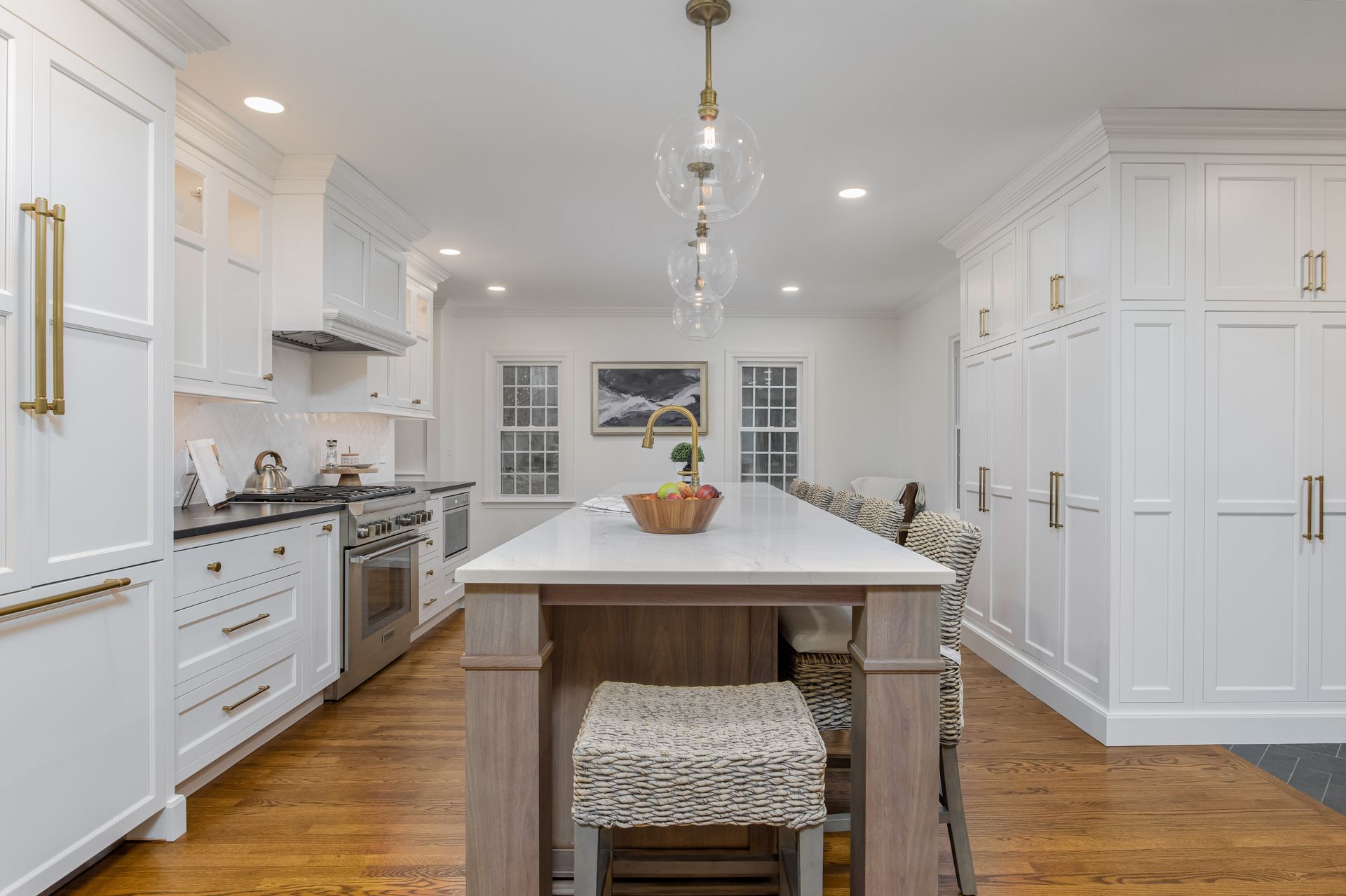 Bright white kitchen with a large island, gold hardware, wood floors, and built-in cabinets.