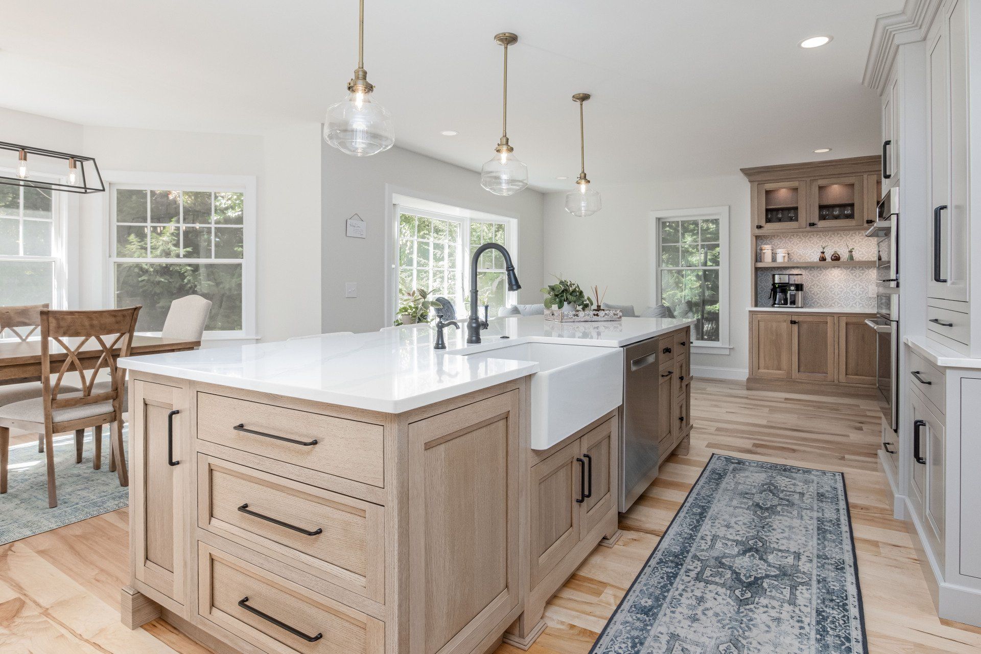 Bright modern kitchen with large island, light wood cabinets, white countertops, and blue rug in open dining space