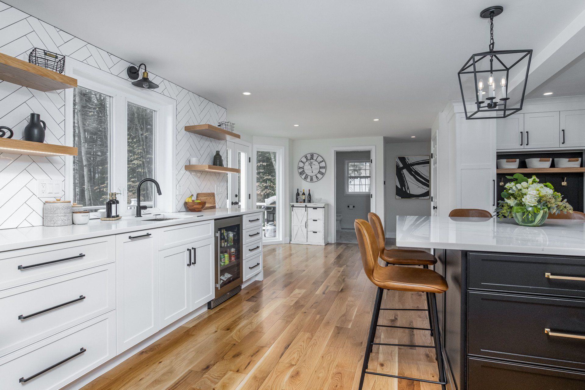 Bright modern kitchen with white cabinets, wood floors, and a black island with bar stools