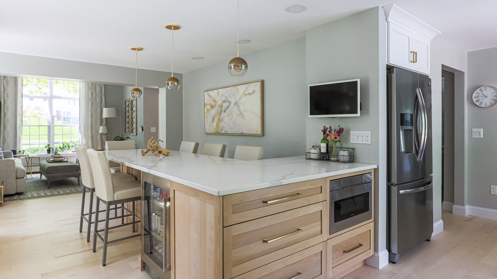 Bright modern kitchen with island, bar stools, stainless fridge, and light blue walls leading to a living area