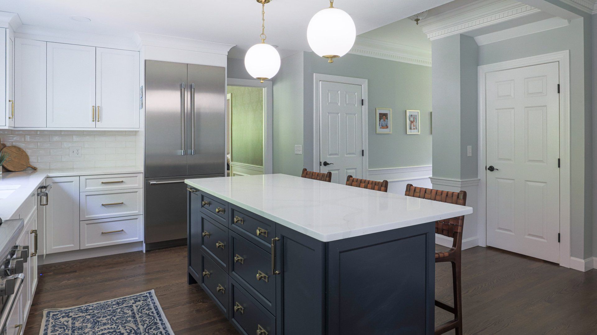 Bright kitchen with gray island, stainless fridge, white cabinets, and pendant lights