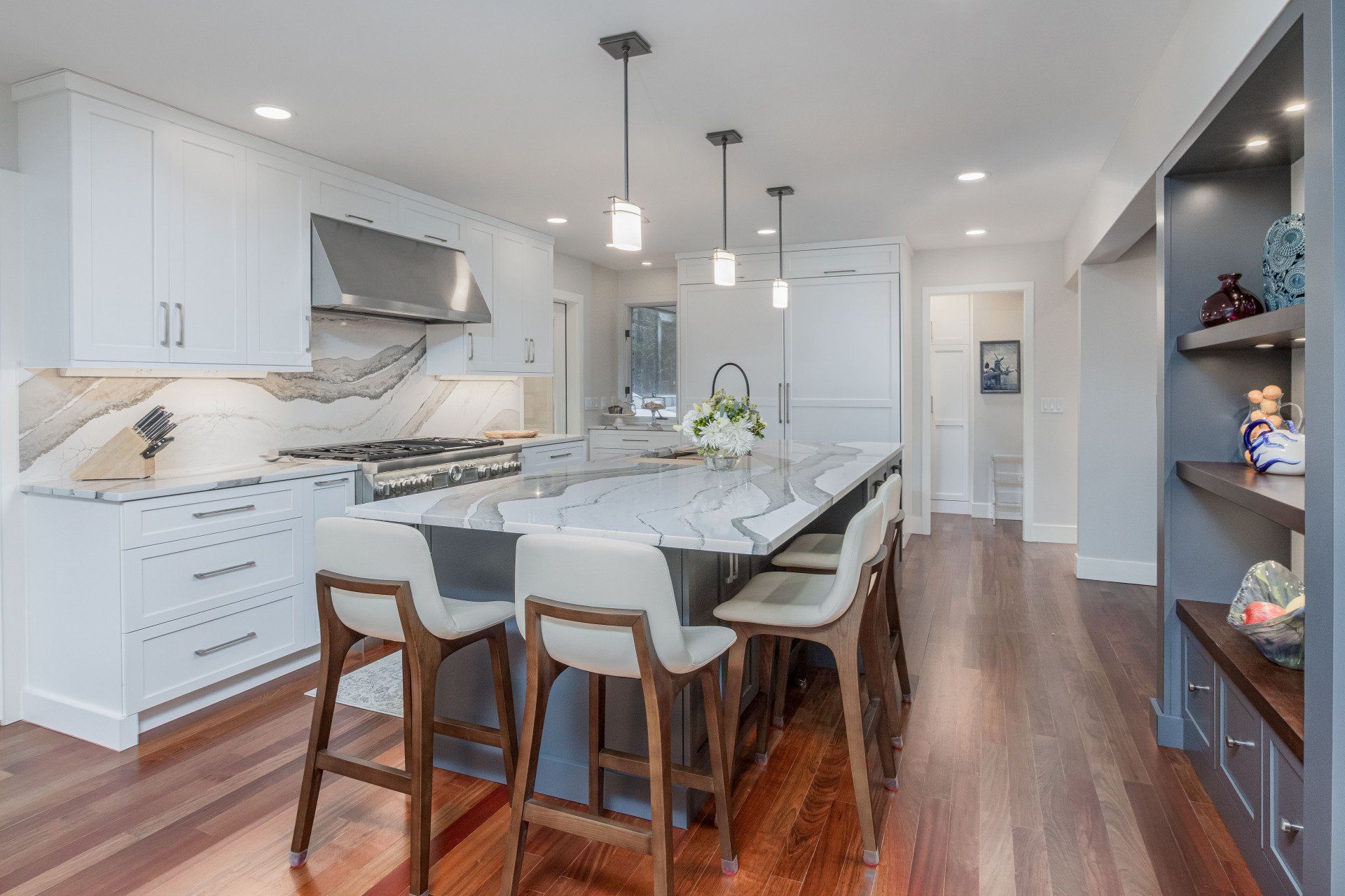 Bright modern kitchen with white cabinets, marble island, barstools, and hardwood floors