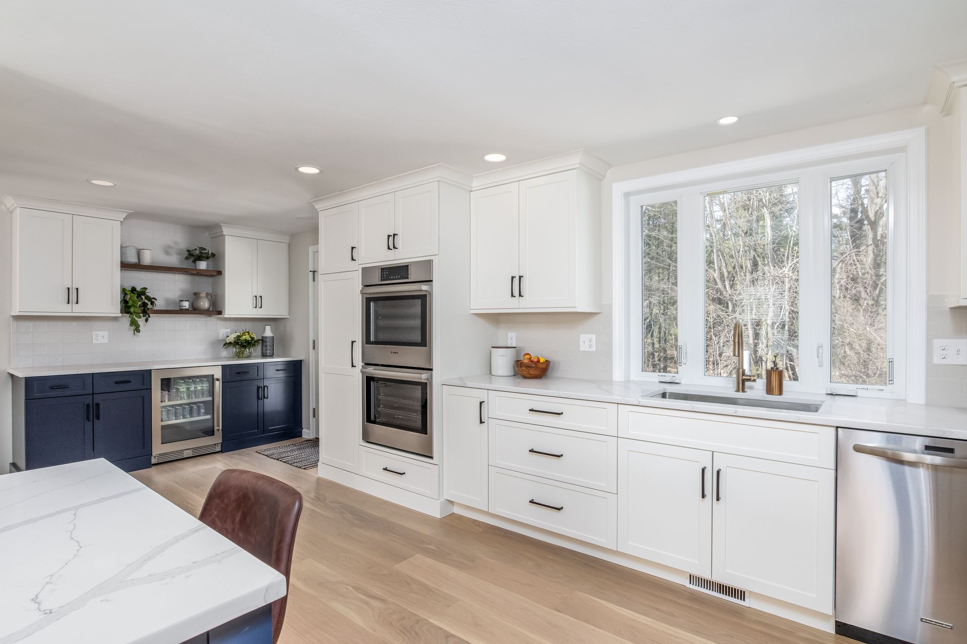 Bright modern kitchen with white cabinets, blue lower cabinets, and large windows over a light wood floor