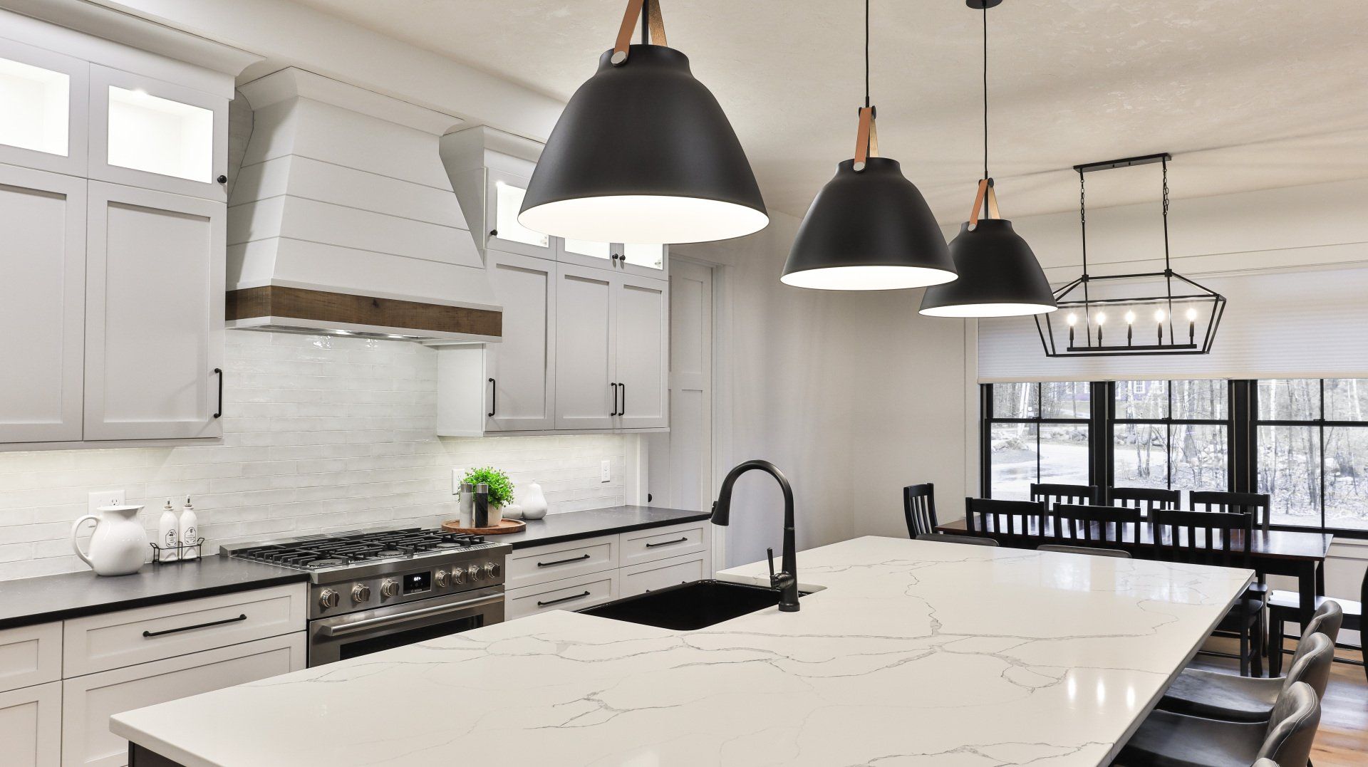 Modern white kitchen with large island, black pendant lights, and stainless steel appliances