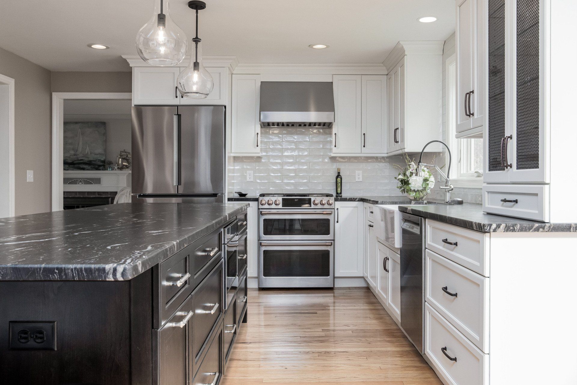 Modern kitchen with stainless steel appliances, dark countertops, white cabinets, and hardwood floors