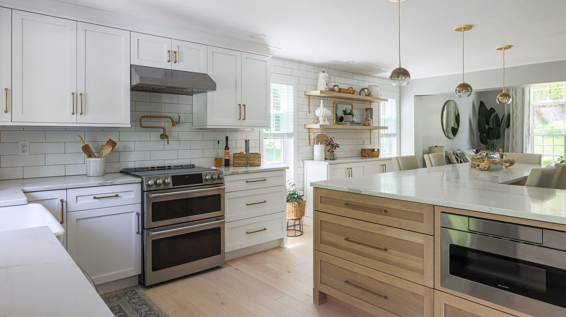 Bright white modern kitchen with large island, stainless stove, and wood accents.