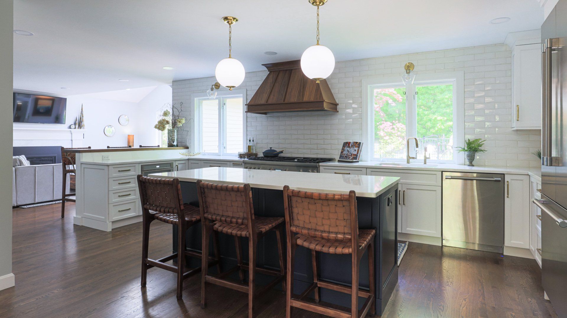 Bright kitchen with island, wicker bar stools, white cabinets, and wood range hood under pendant lights.