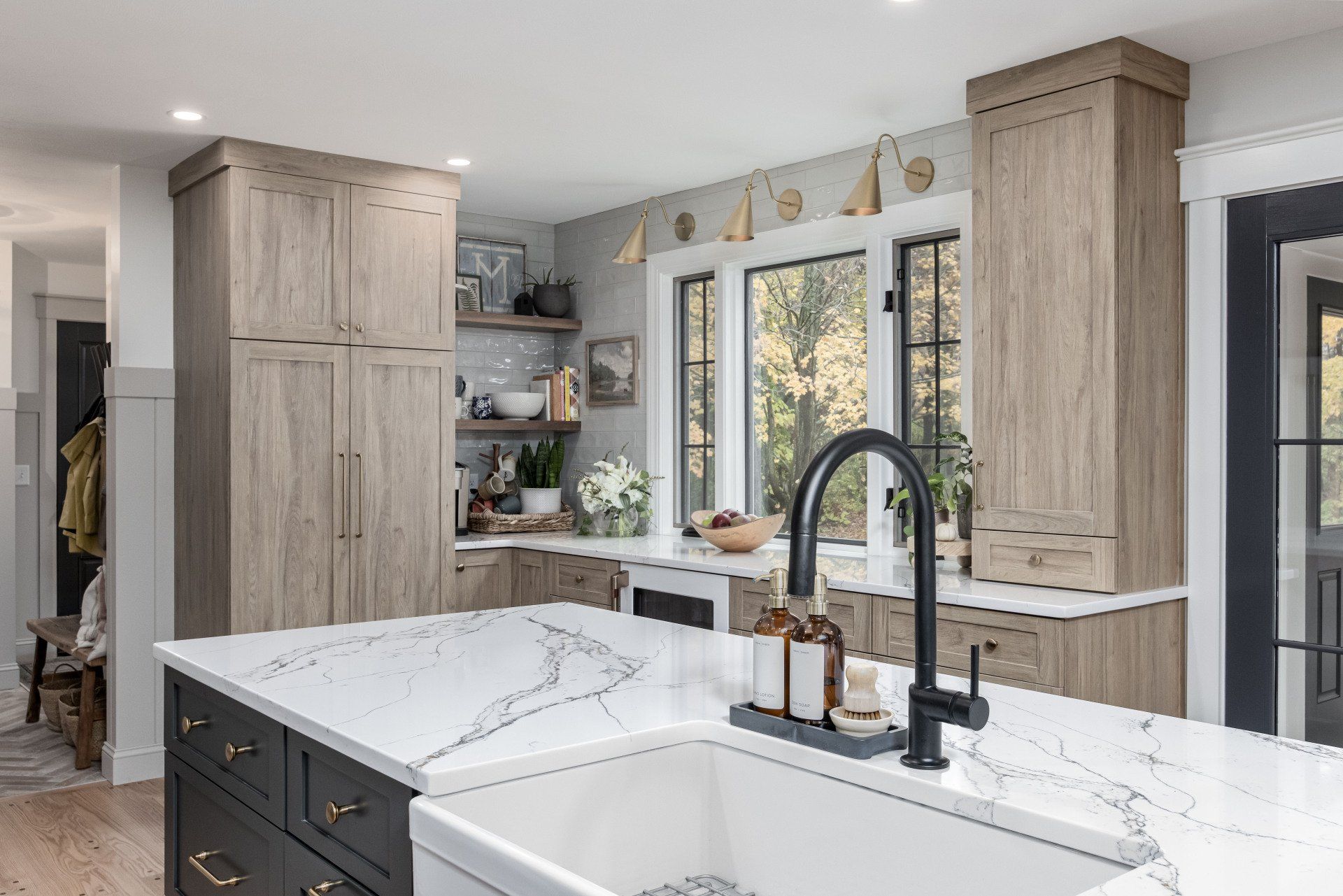 Modern kitchen with white marble island, black faucet, light wood cabinets, and large windows