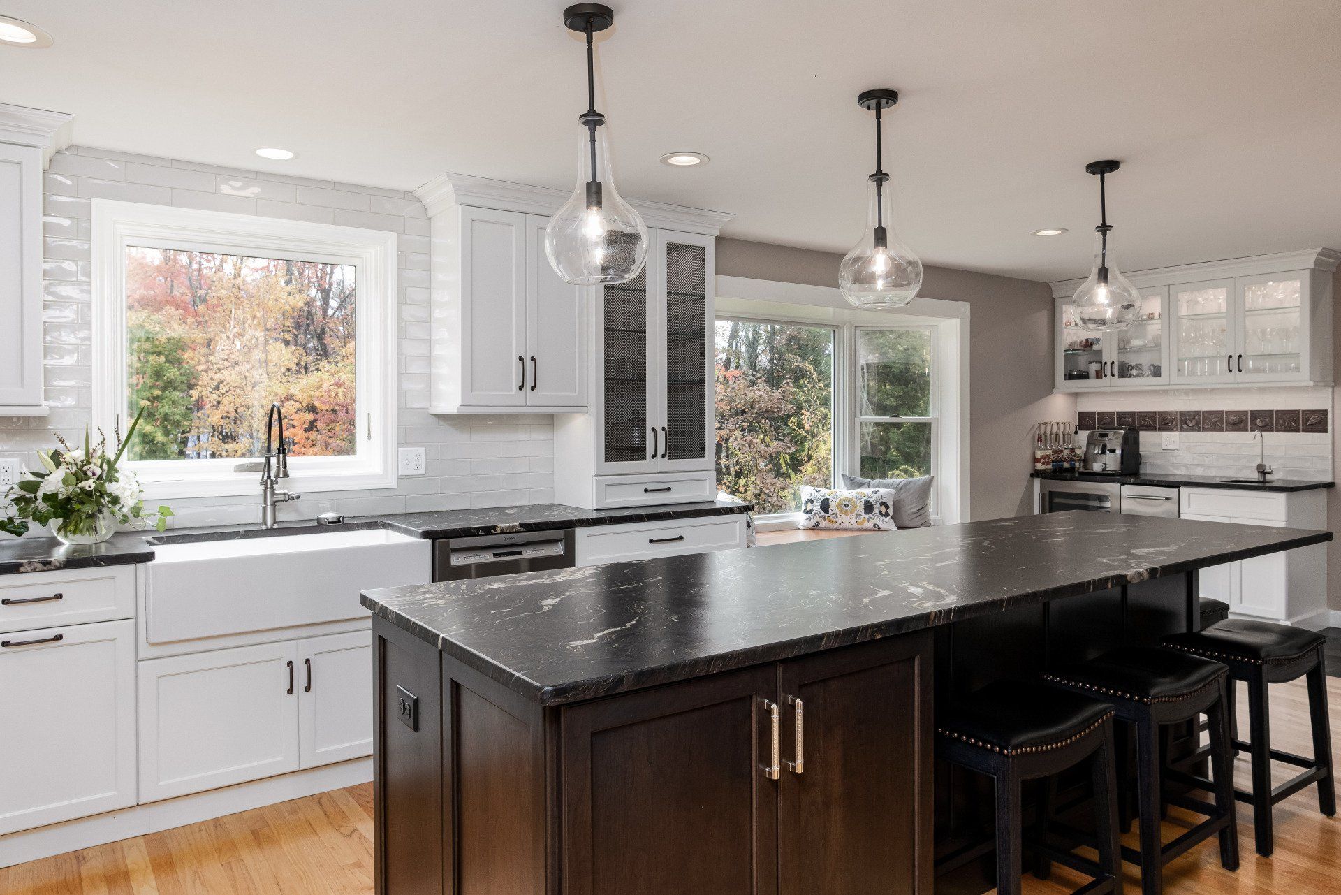 Bright modern kitchen with white cabinets, black island, pendant lights, and large windows