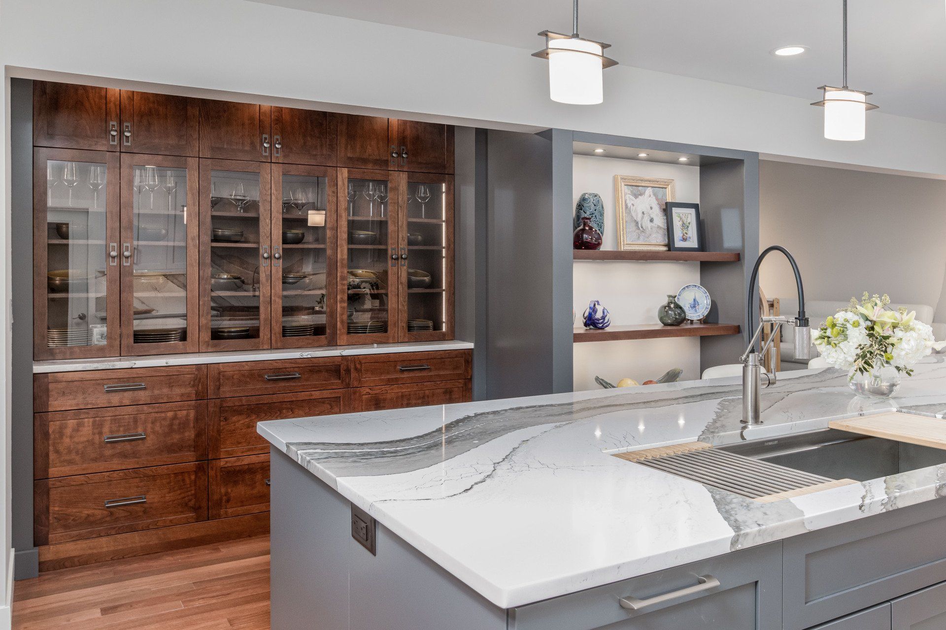 Modern kitchen with white island, gray cabinets, wood built-in hutch, and pendant lights