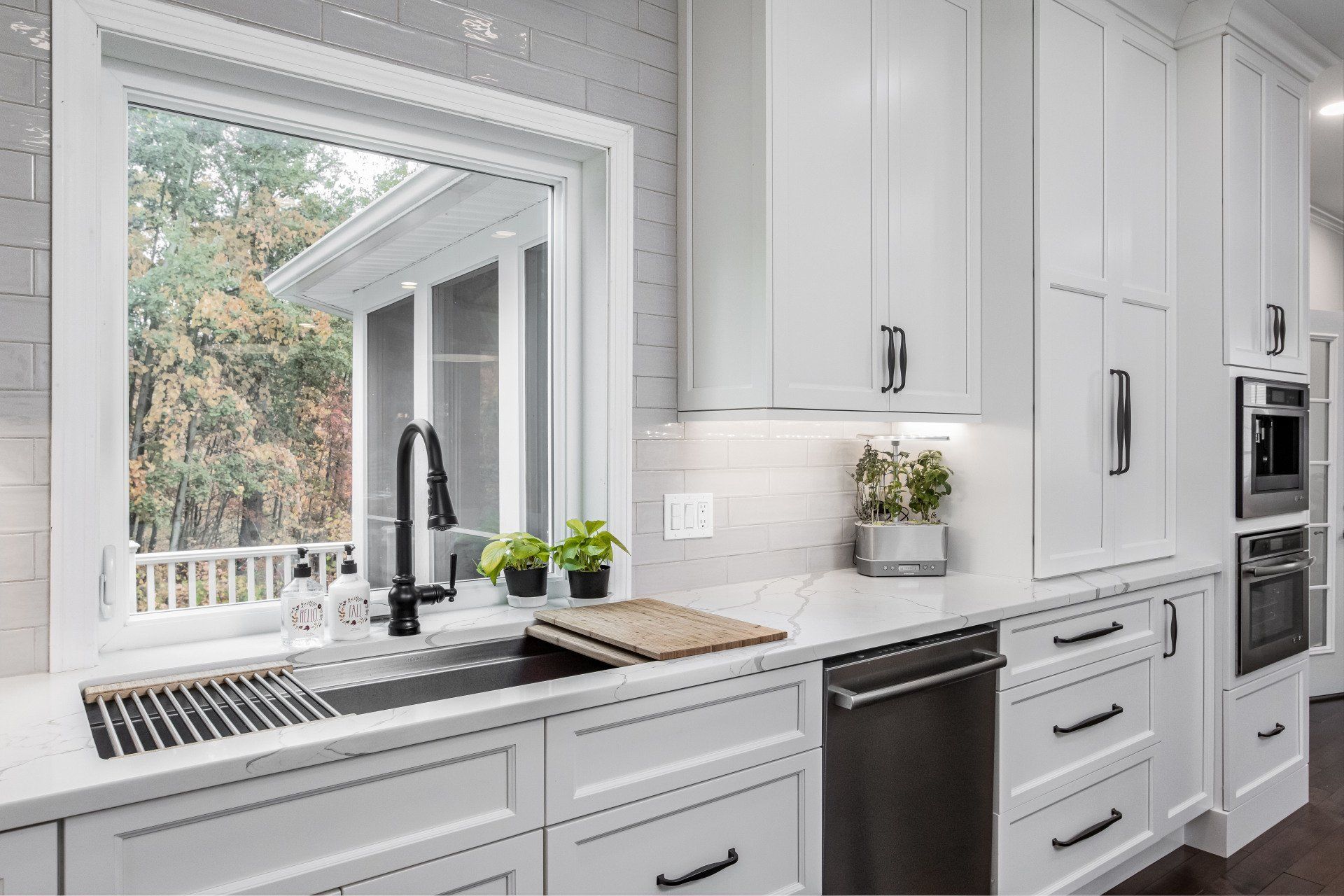 Bright white kitchen with a window over the sink, black faucet, and built-in dishwasher.