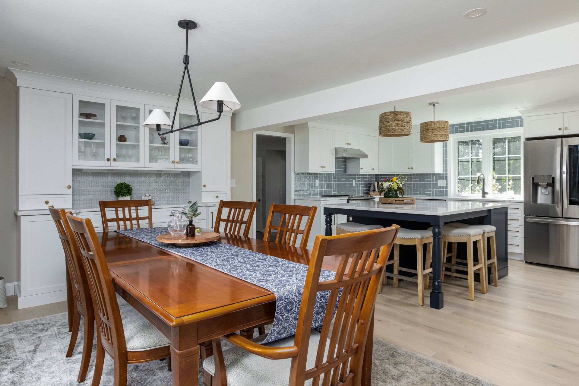 Bright dining and kitchen area with wooden table, chairs, and gray island in a white home interior