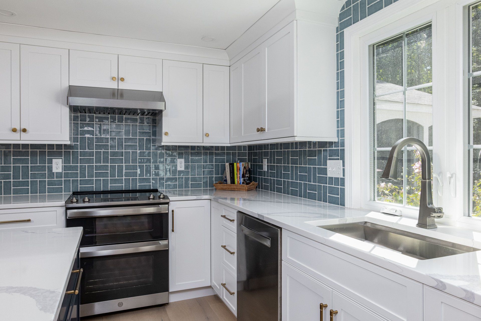 Bright white kitchen with blue tile backsplash, black stove, and window over the sink.
