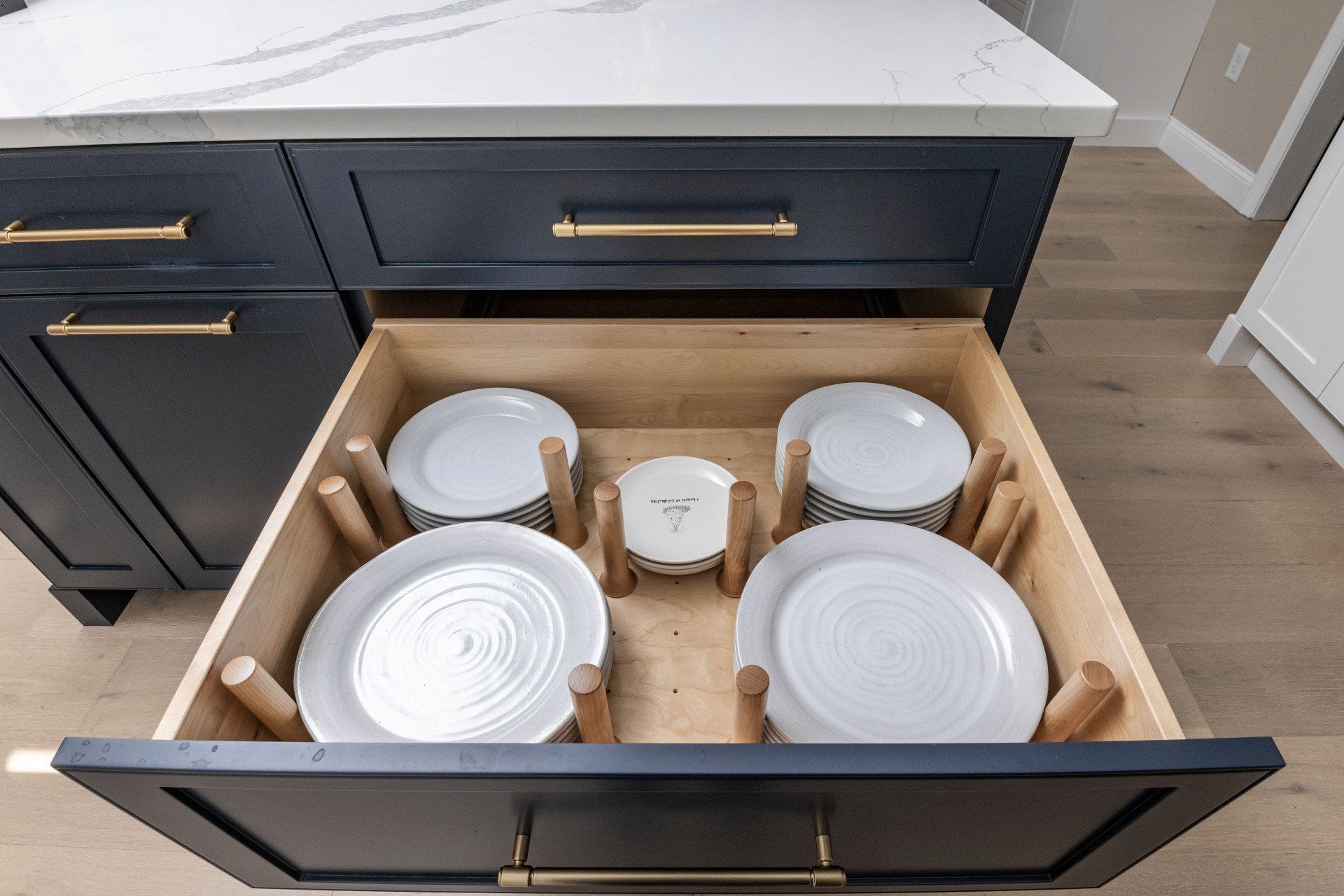 Open drawer under kitchen sink with neatly stored white dishes and bowls in organizers