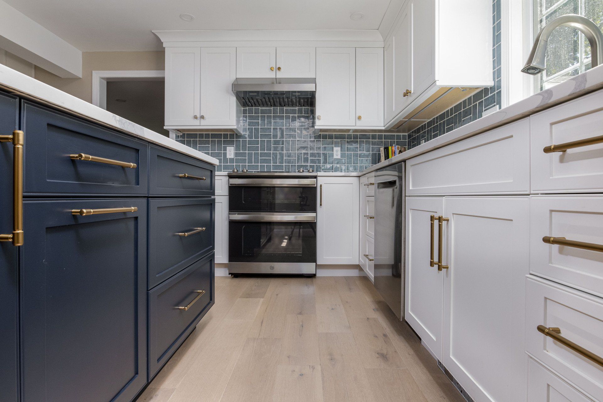 Modern kitchen with white and navy cabinets, gold hardware, wood floor, and stainless steel appliances