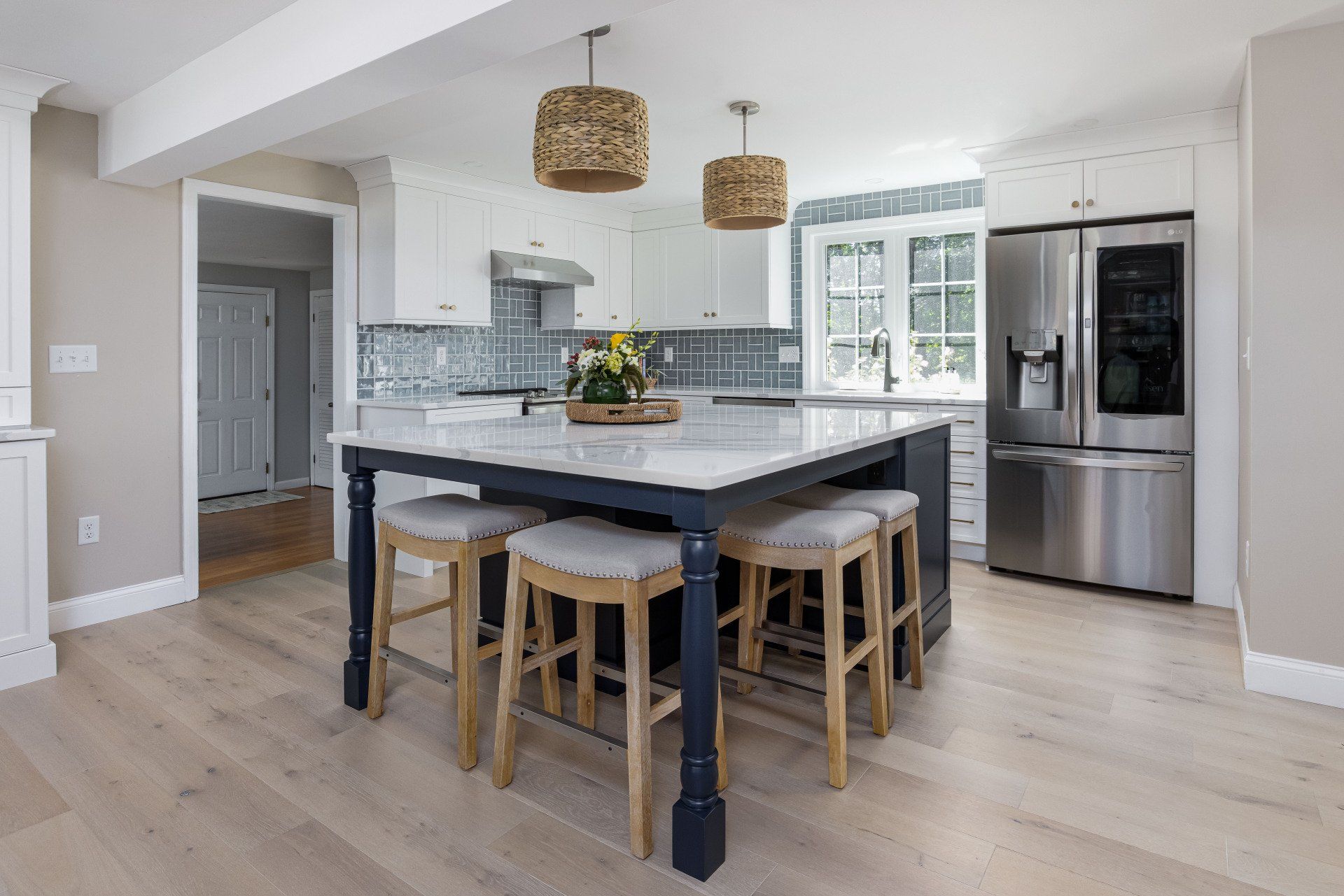 Modern white kitchen with island, stools, pendant lights, and stainless steel appliances