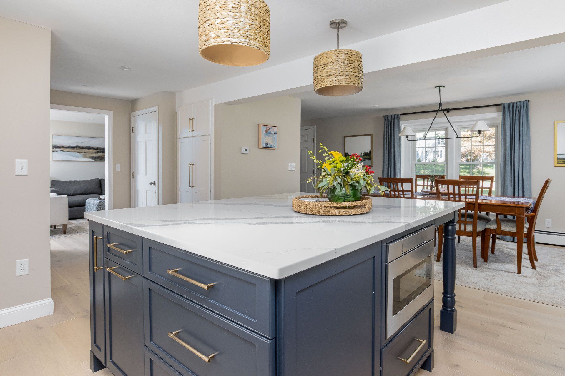 Modern kitchen with a large island, dark cabinets, pendant lights, and a dining area beyond.