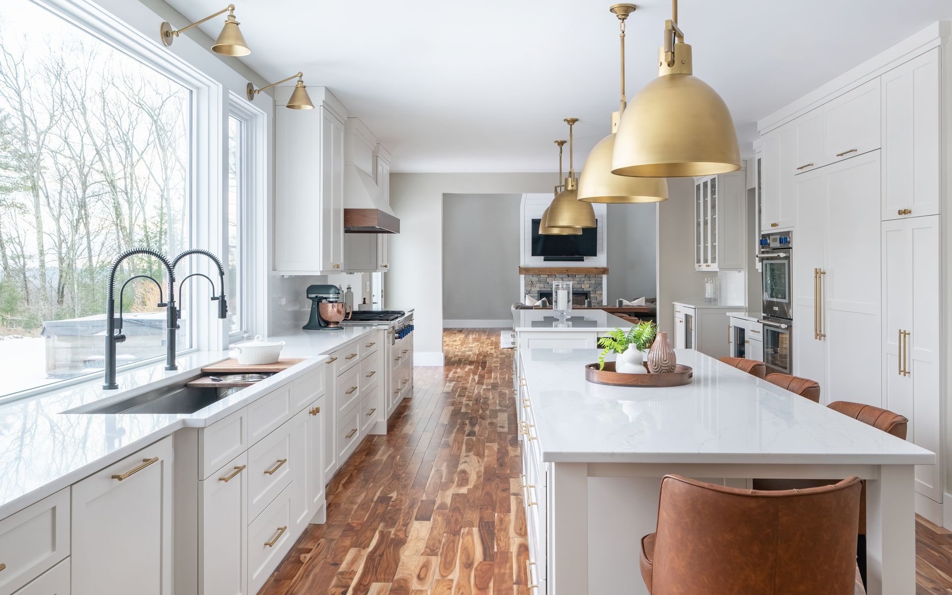 Bright white kitchen with brass pendants, large island, and sunlit windows.
