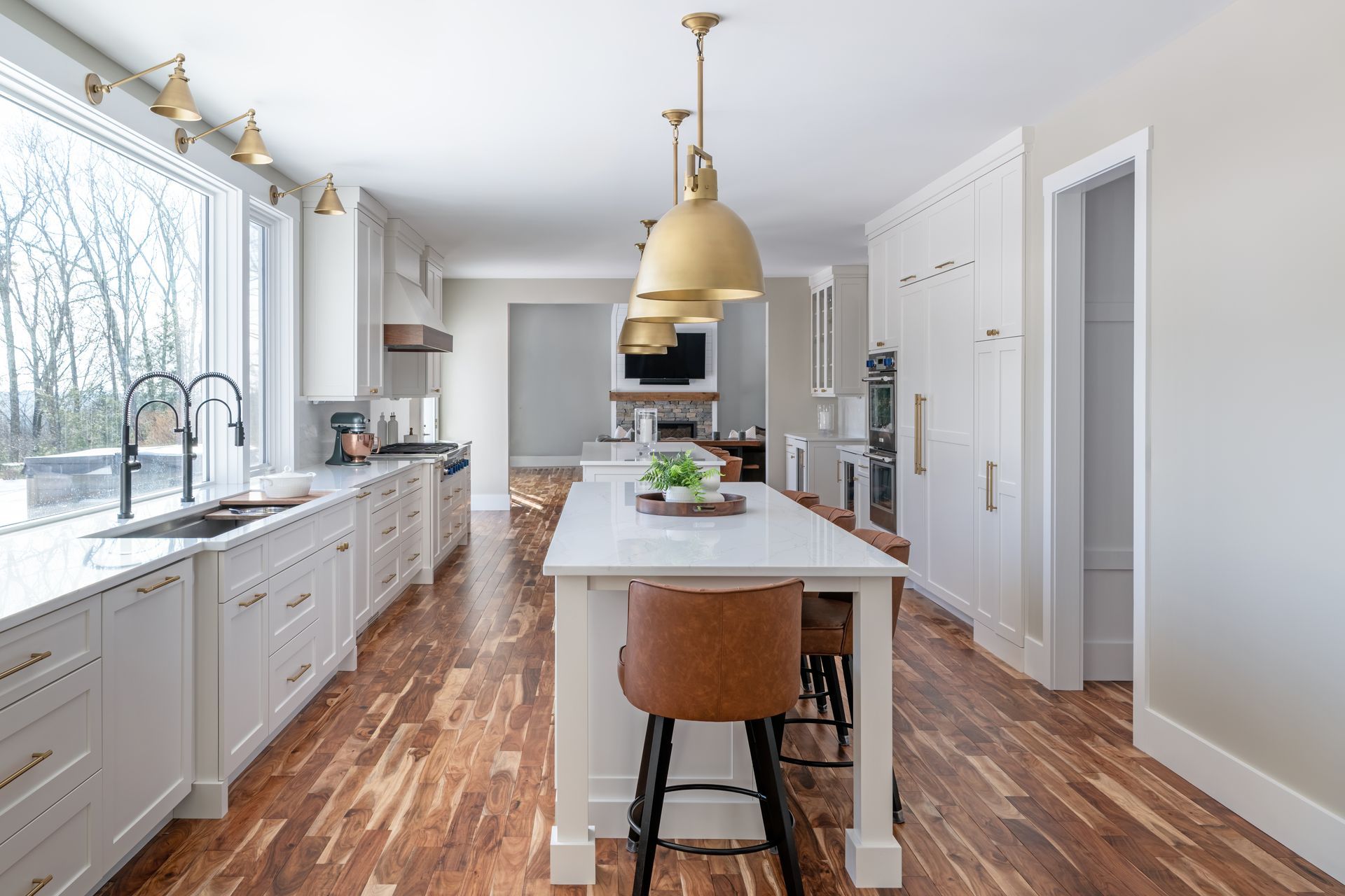 Bright modern kitchen with white cabinets, wood floors, central island, and brass pendant lights