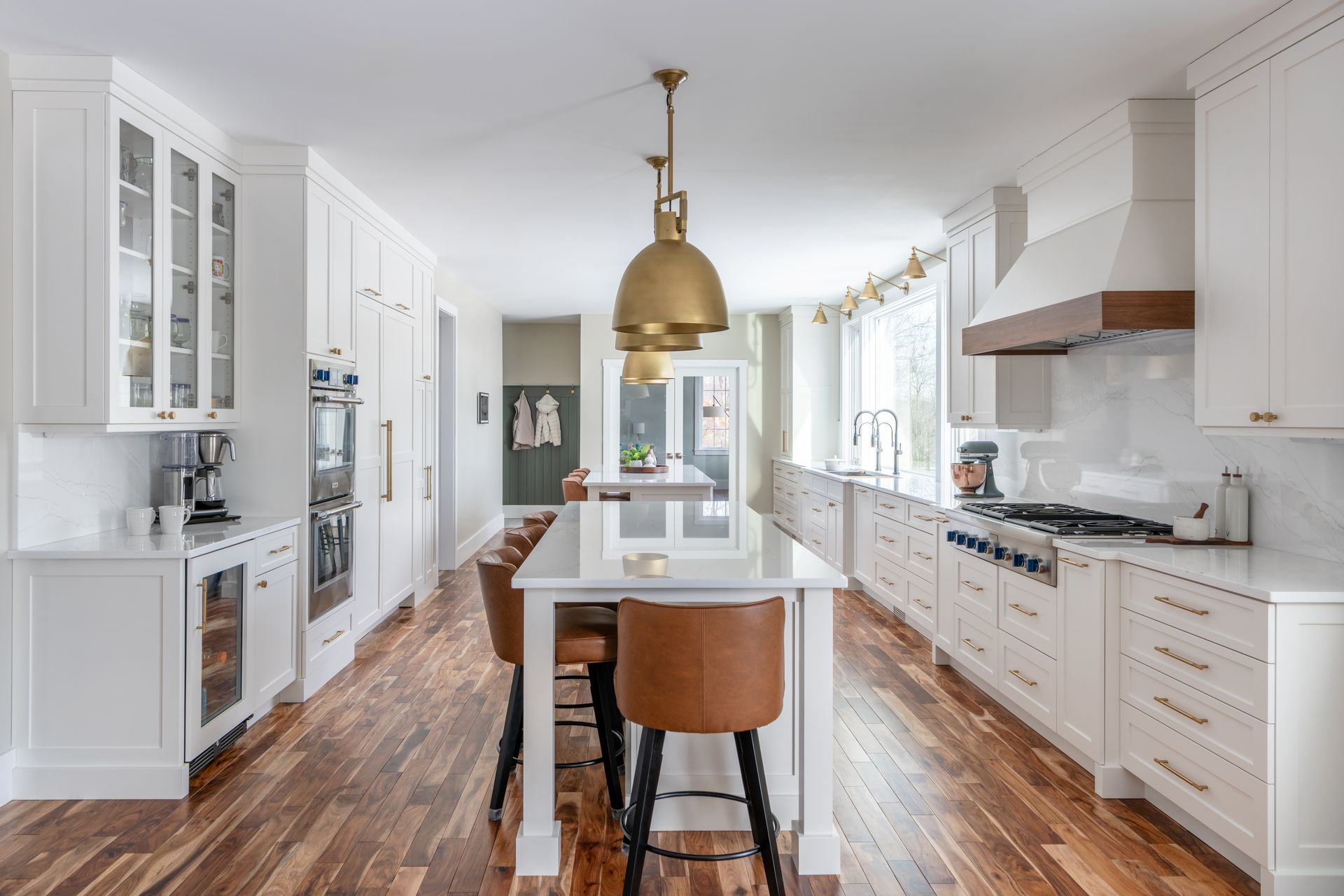 Bright white modern kitchen with wood floors, island, brass pendant light, and large windows