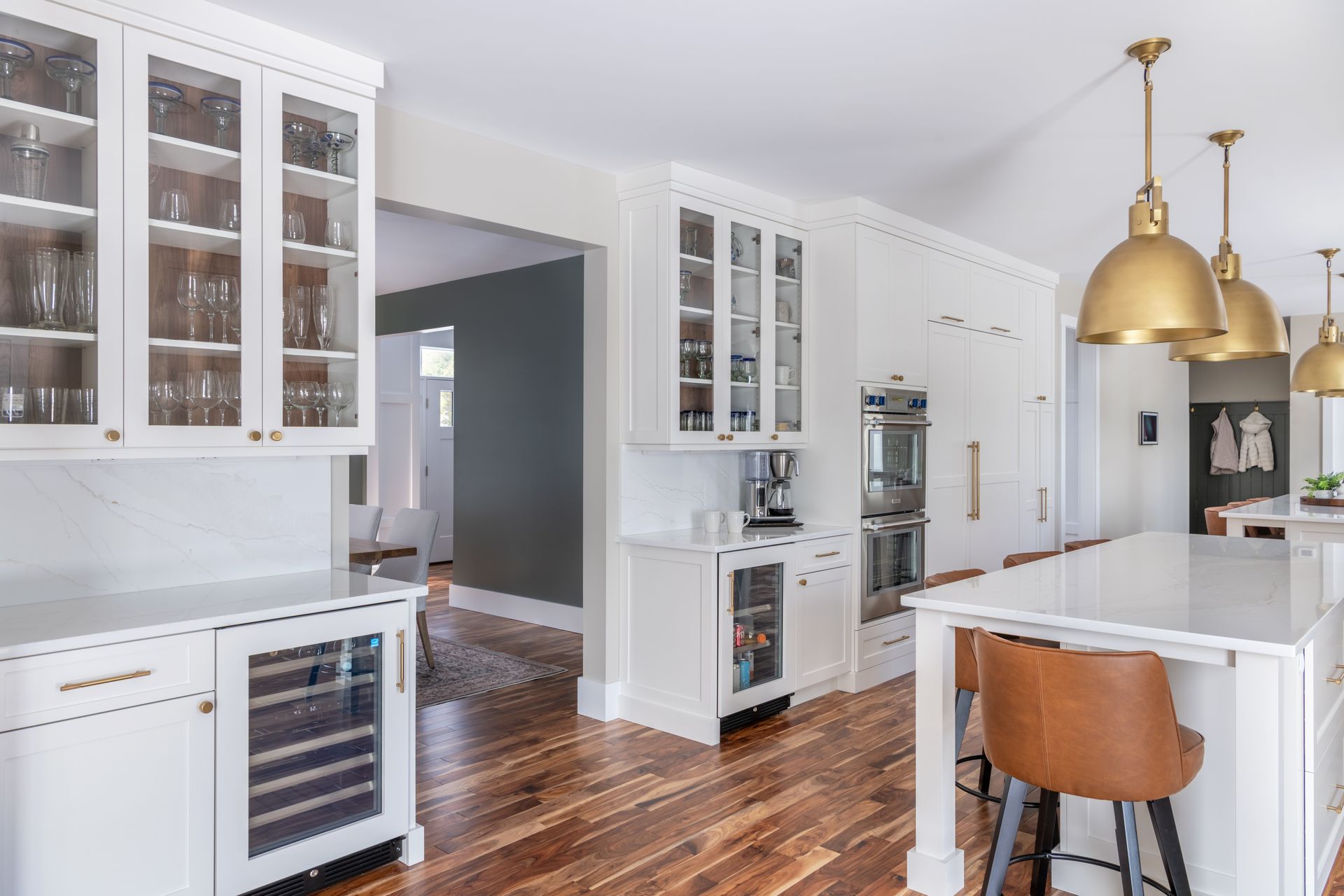 Bright white kitchen with glass cabinets, hardwood floors, and a marble island with brass pendant lights.