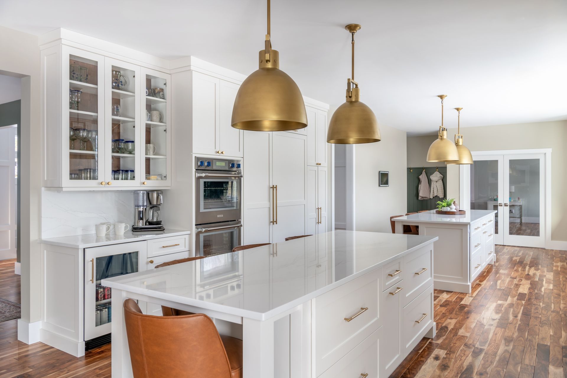 Bright white kitchen with gold pendant lights, island, cabinets, and wood floors