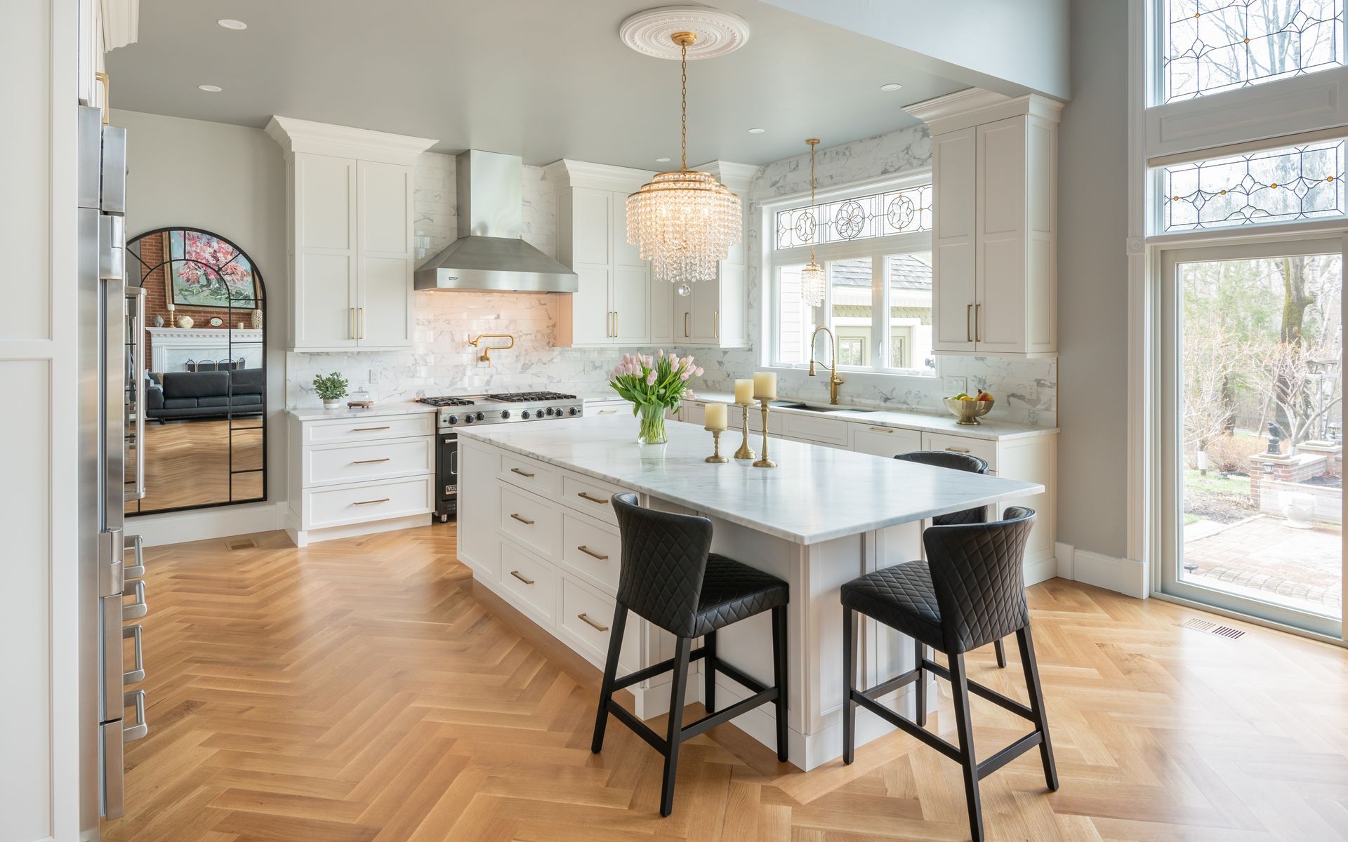 Bright modern kitchen with white island, black stools, herringbone wood floor, and large windows
