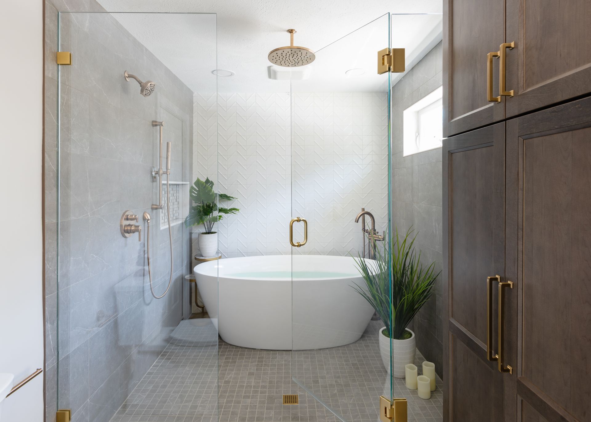 Modern bathroom with a freestanding tub, glass shower, gray tile, and wood cabinets