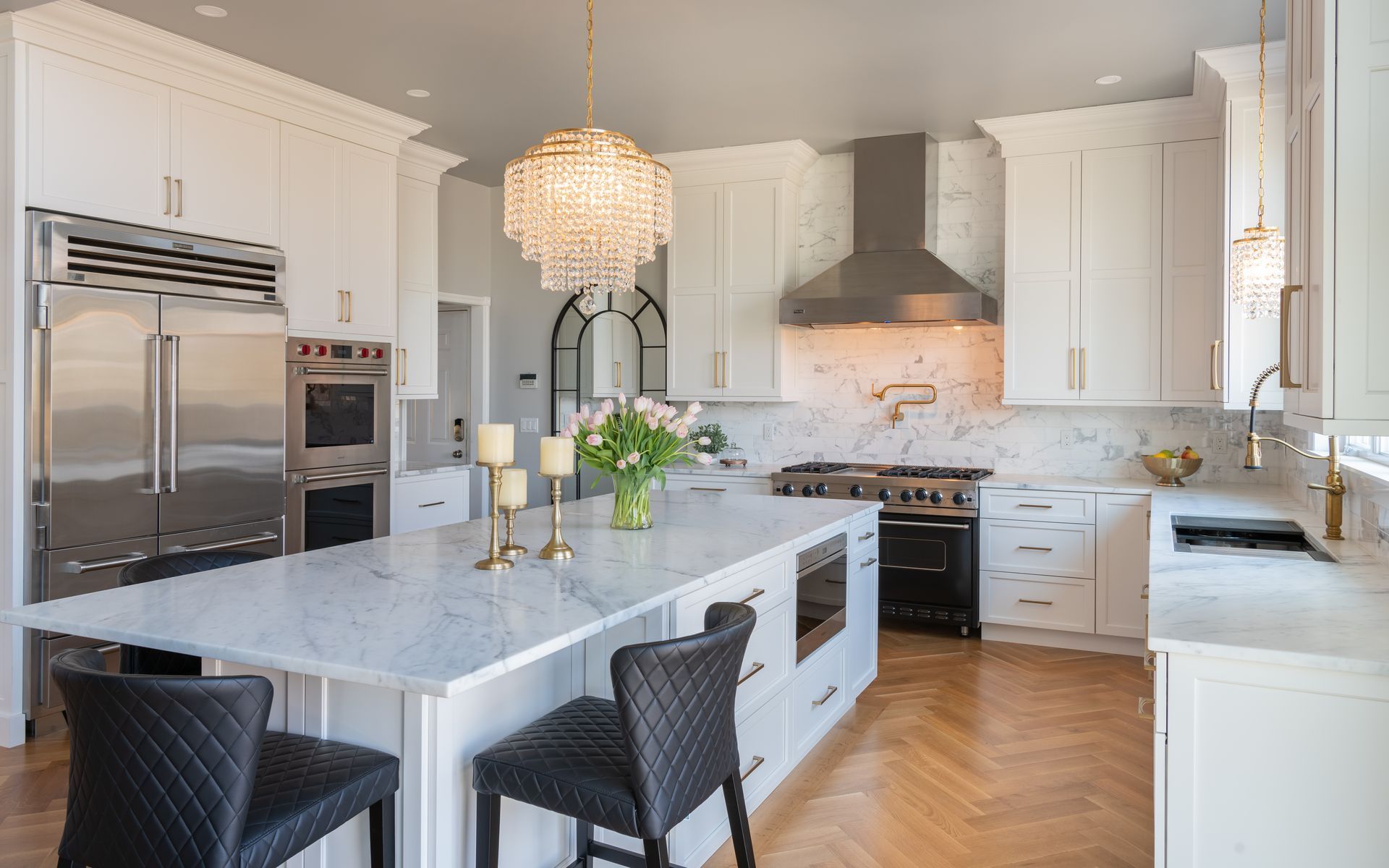 Bright modern kitchen with white cabinets, marble island, stainless appliances, and two black bar stools.