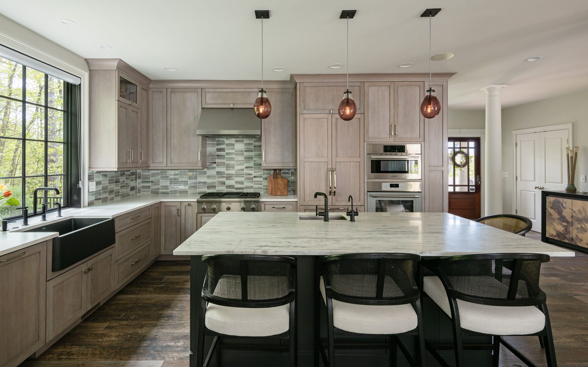 Modern kitchen with large island, light wood cabinets, marble countertops, and pendant lights